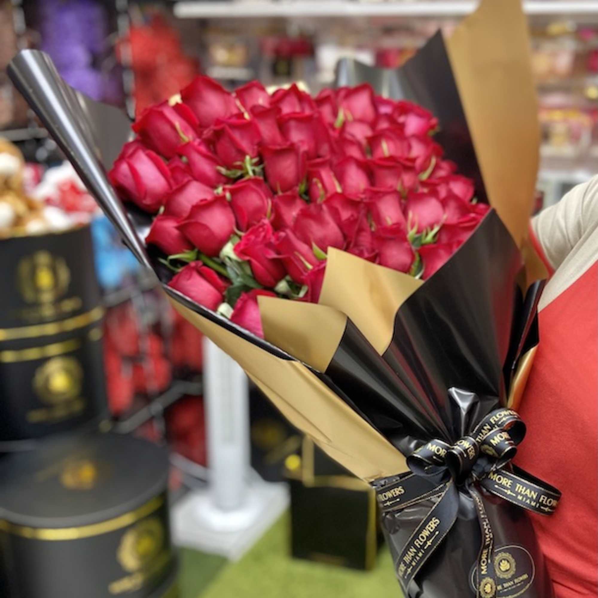 Large bouquet of red roses wrapped in black and gold paper with a branded ribbon