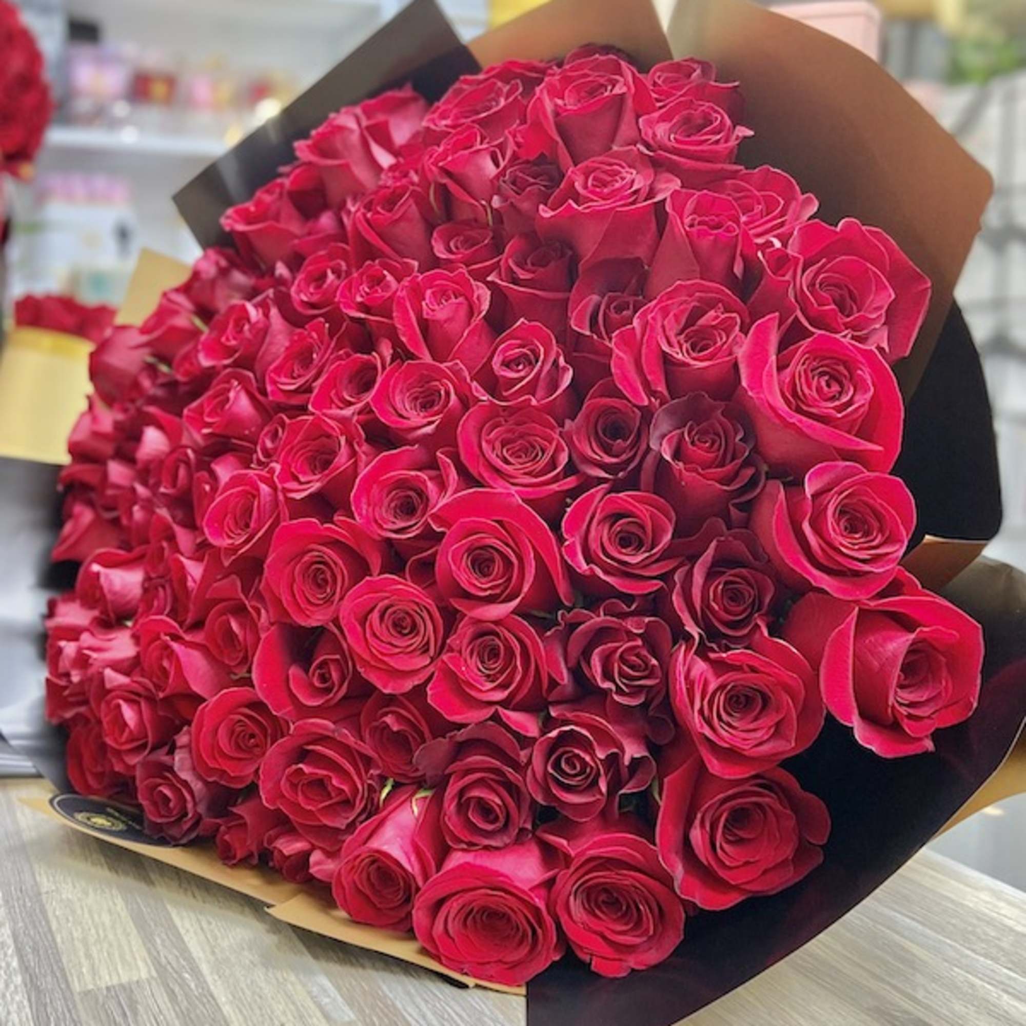 Large wrapped bouquet of tightly clustered red roses resting on a wooden surface