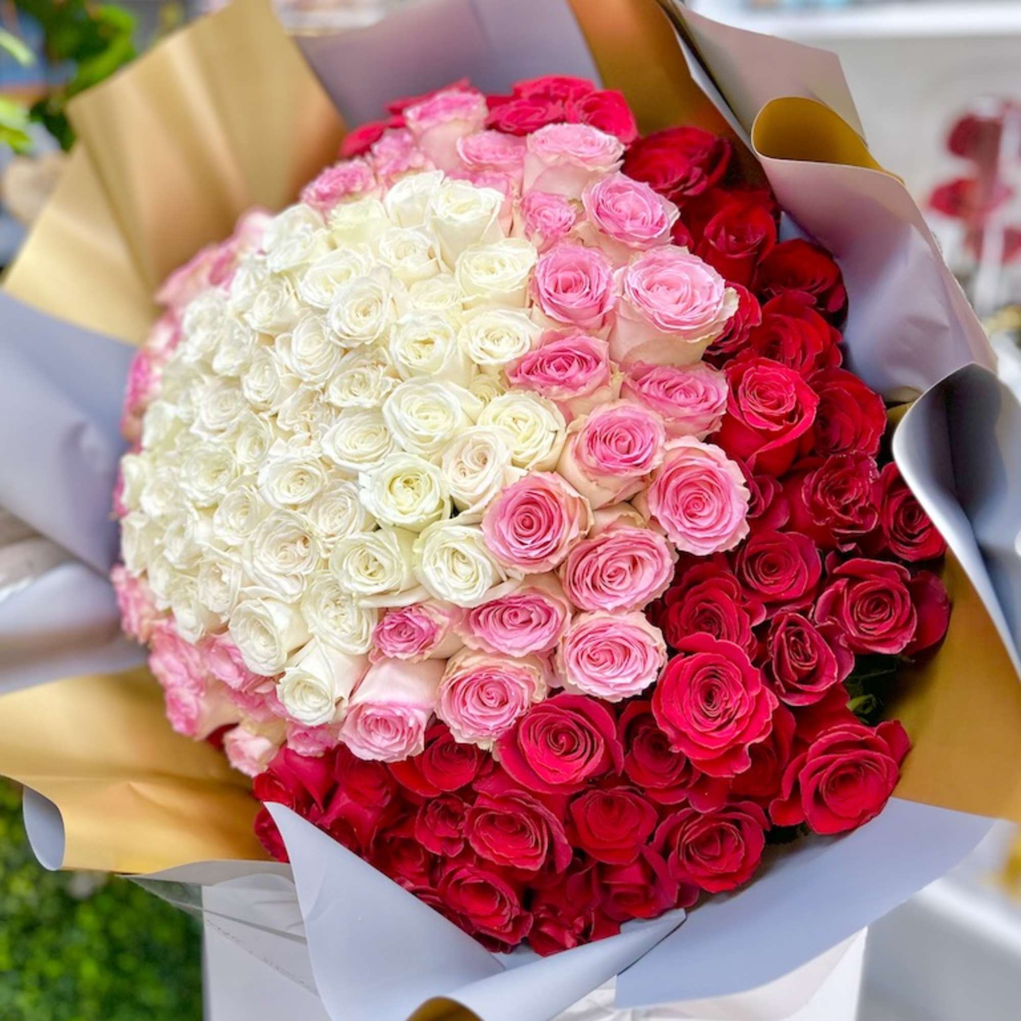 Large round bouquet of white, pink, and red roses wrapped in gold and gray paper