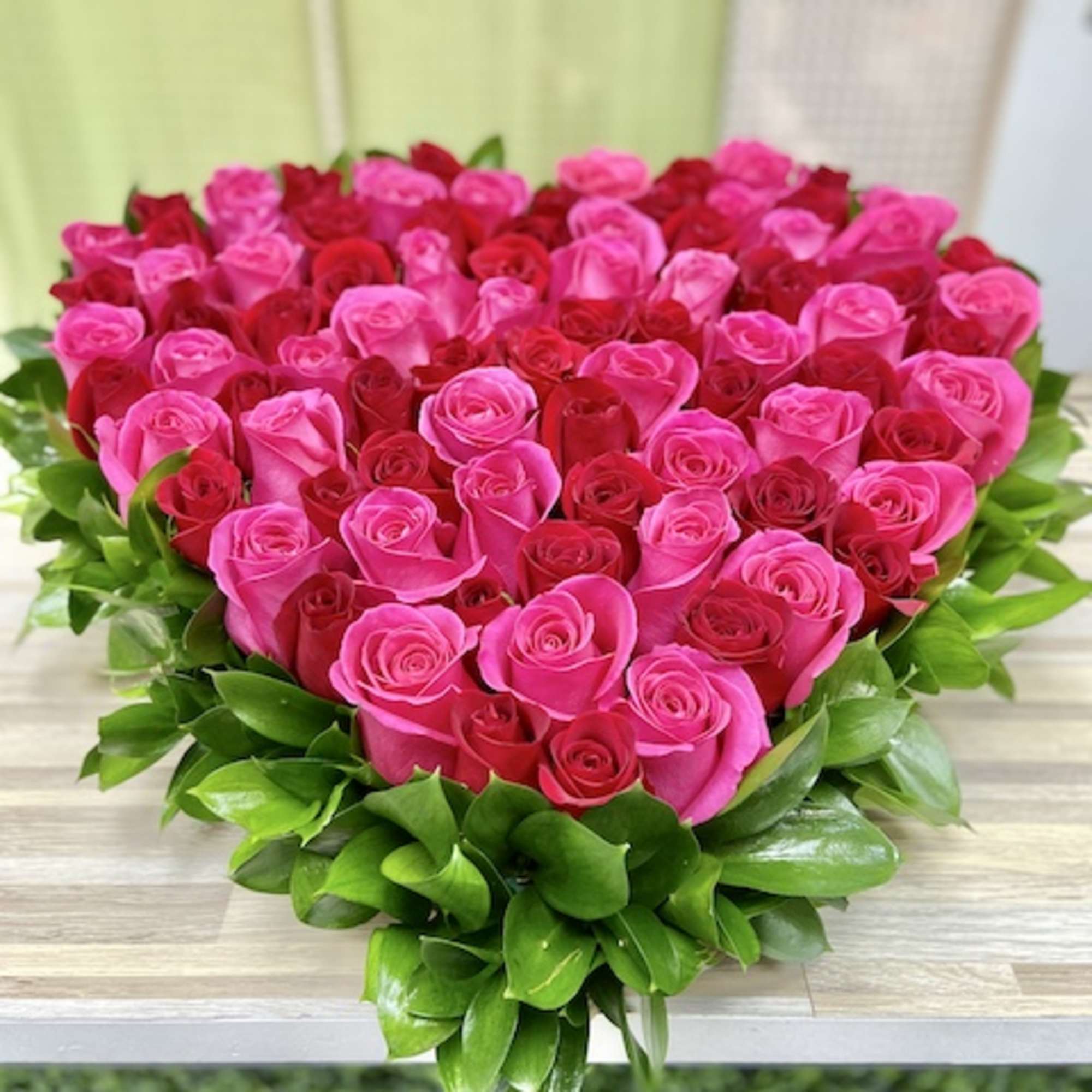 Heart-shaped arrangement of pink and red roses edged with glossy green foliage