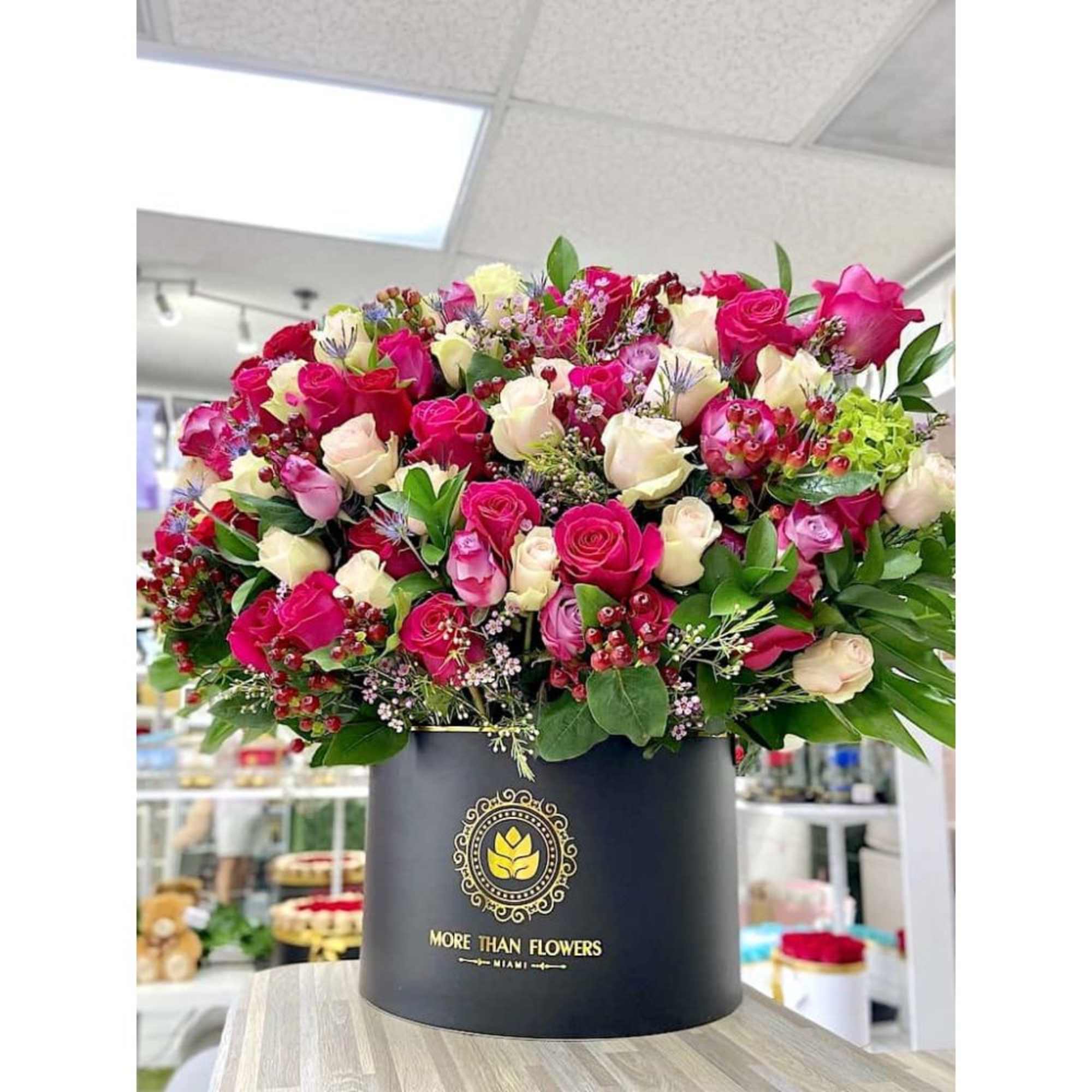 Large hat box arrangement of hot pink, red, and cream roses in a black cylinder container