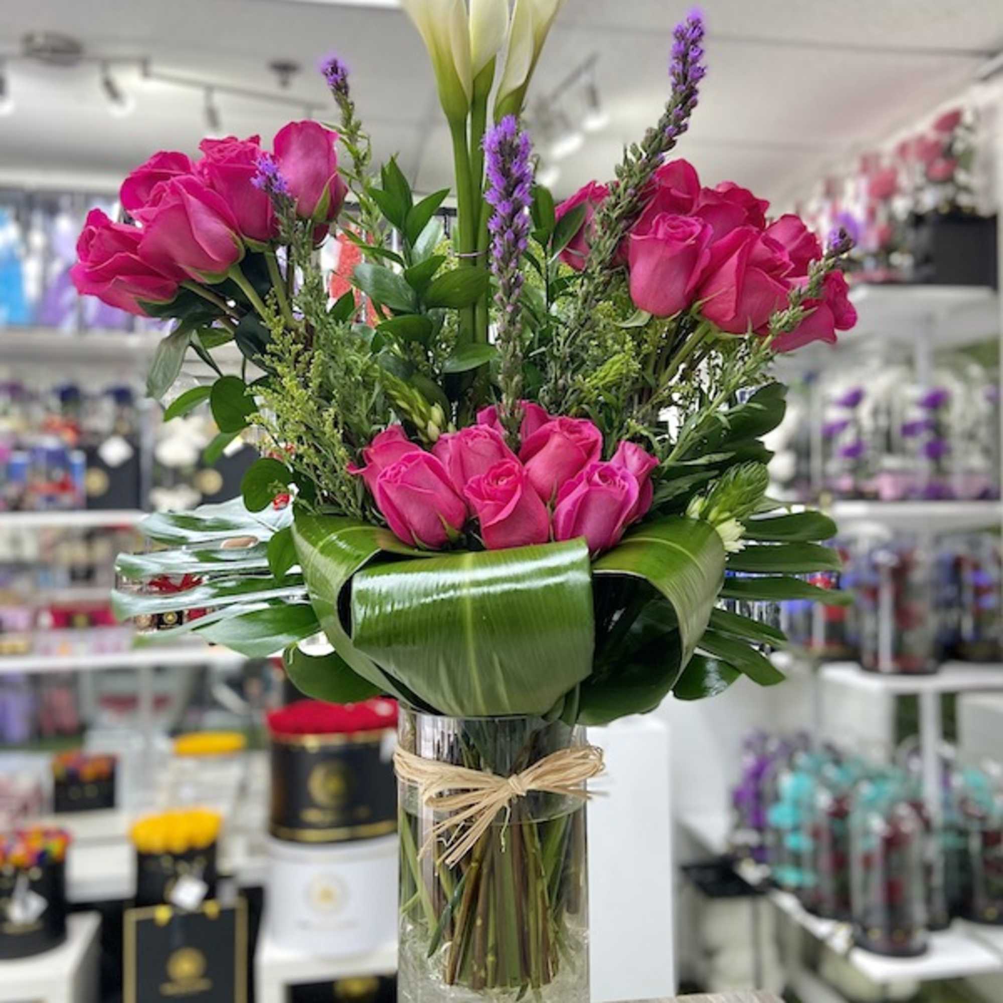 Tall arrangement of hot pink roses and white calla lilies in a clear glass vase with a collar of broad green leaves