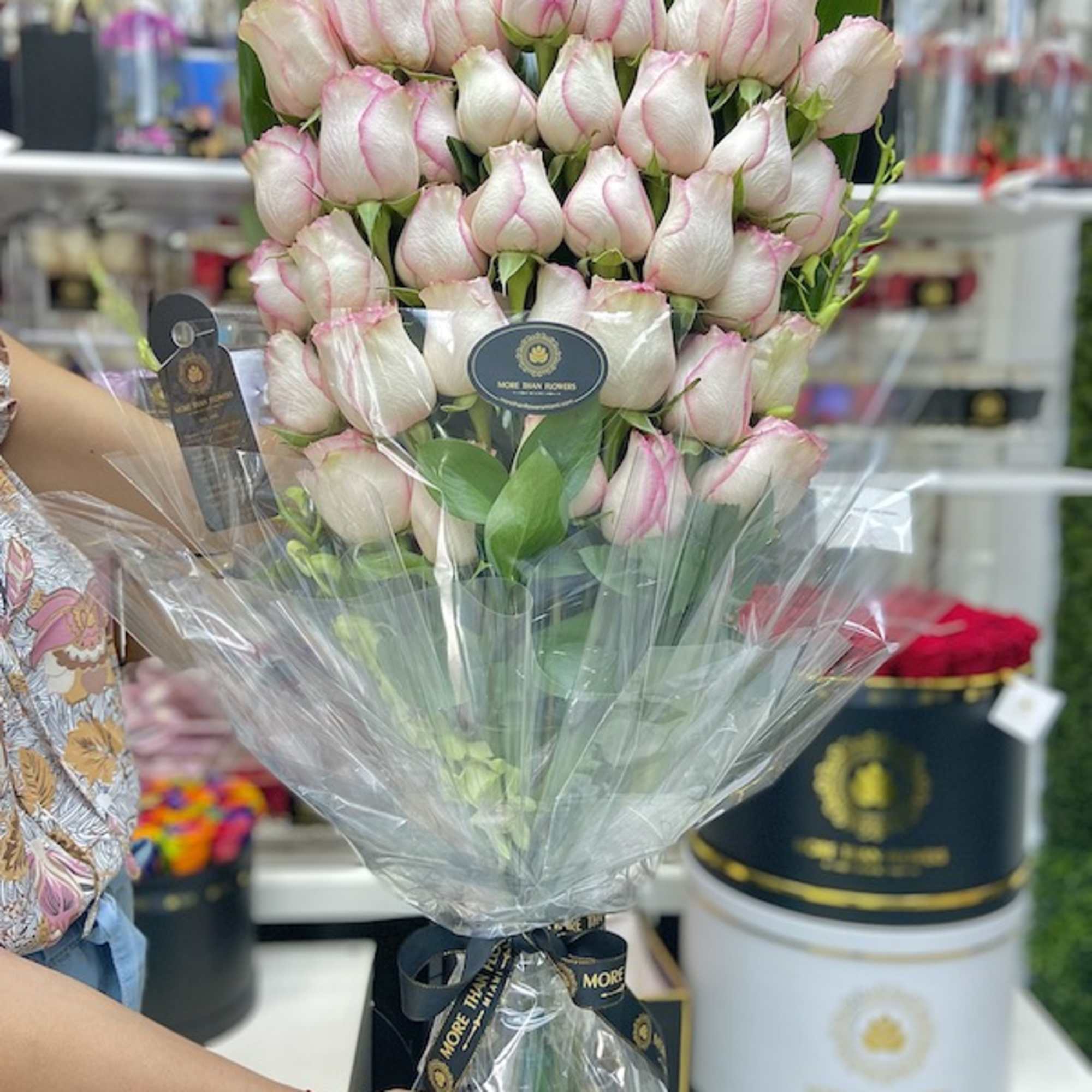 Tall bouquet of white roses with pink edges wrapped in cellophane and tied to a black hat box.