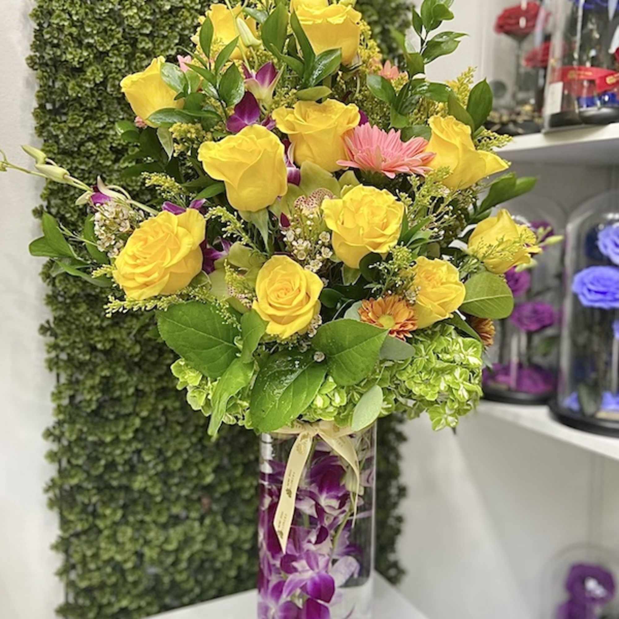 Tall glass vase of yellow roses with mixed bright flowers and submerged purple orchids
