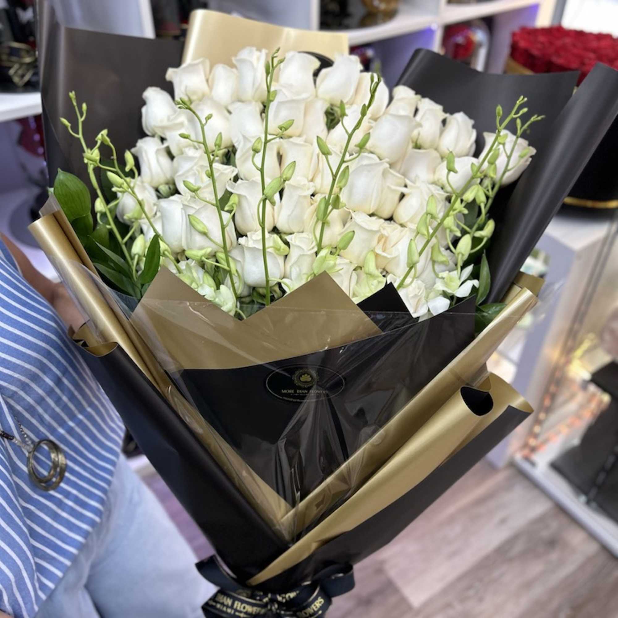Tall bouquet of white roses with green orchid buds wrapped in black and gold paper