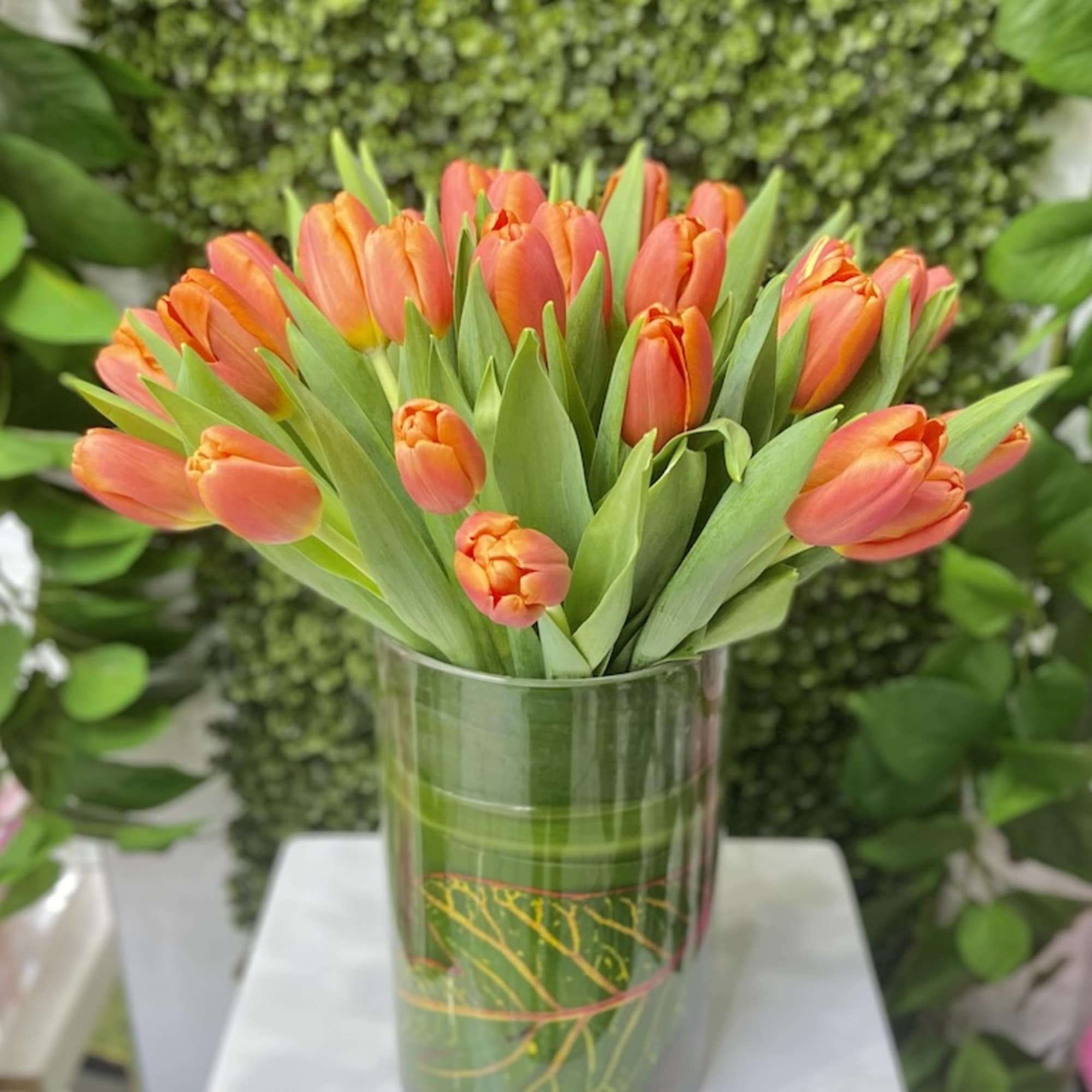 Orange tulips arranged in a tall leaf-wrapped glass cylinder vase