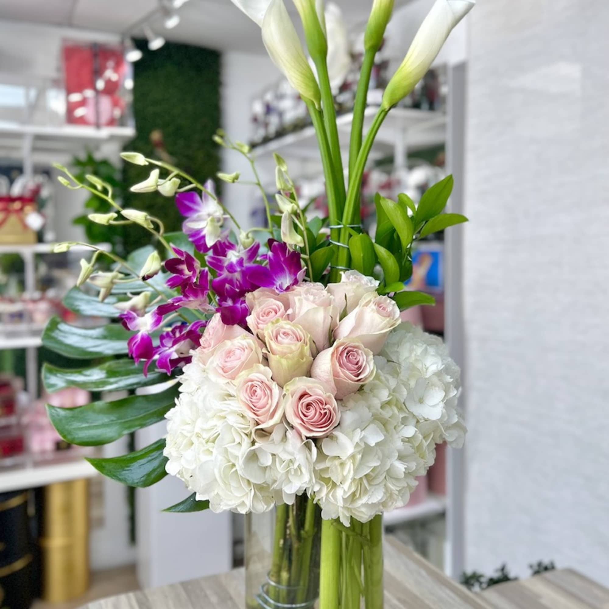 Tall vase arrangement with white hydrangeas, pink roses, purple orchids, and white calla lilies
