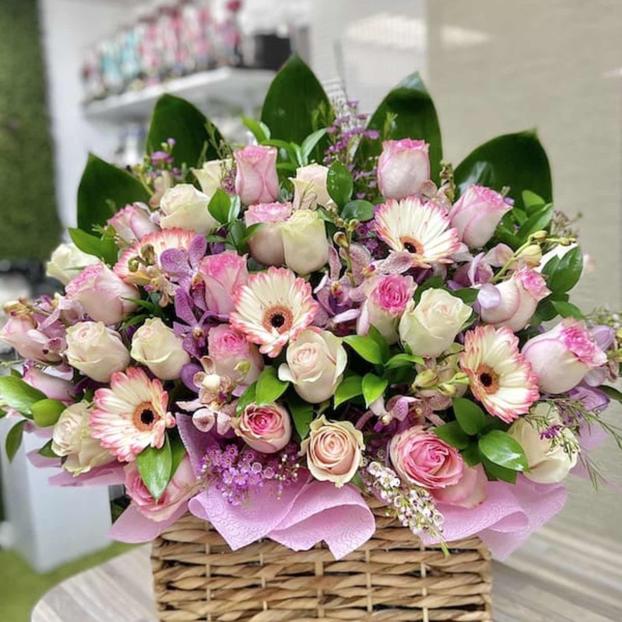 Low basket arrangement of pink and cream roses with pink gerbera daisies and orchids.