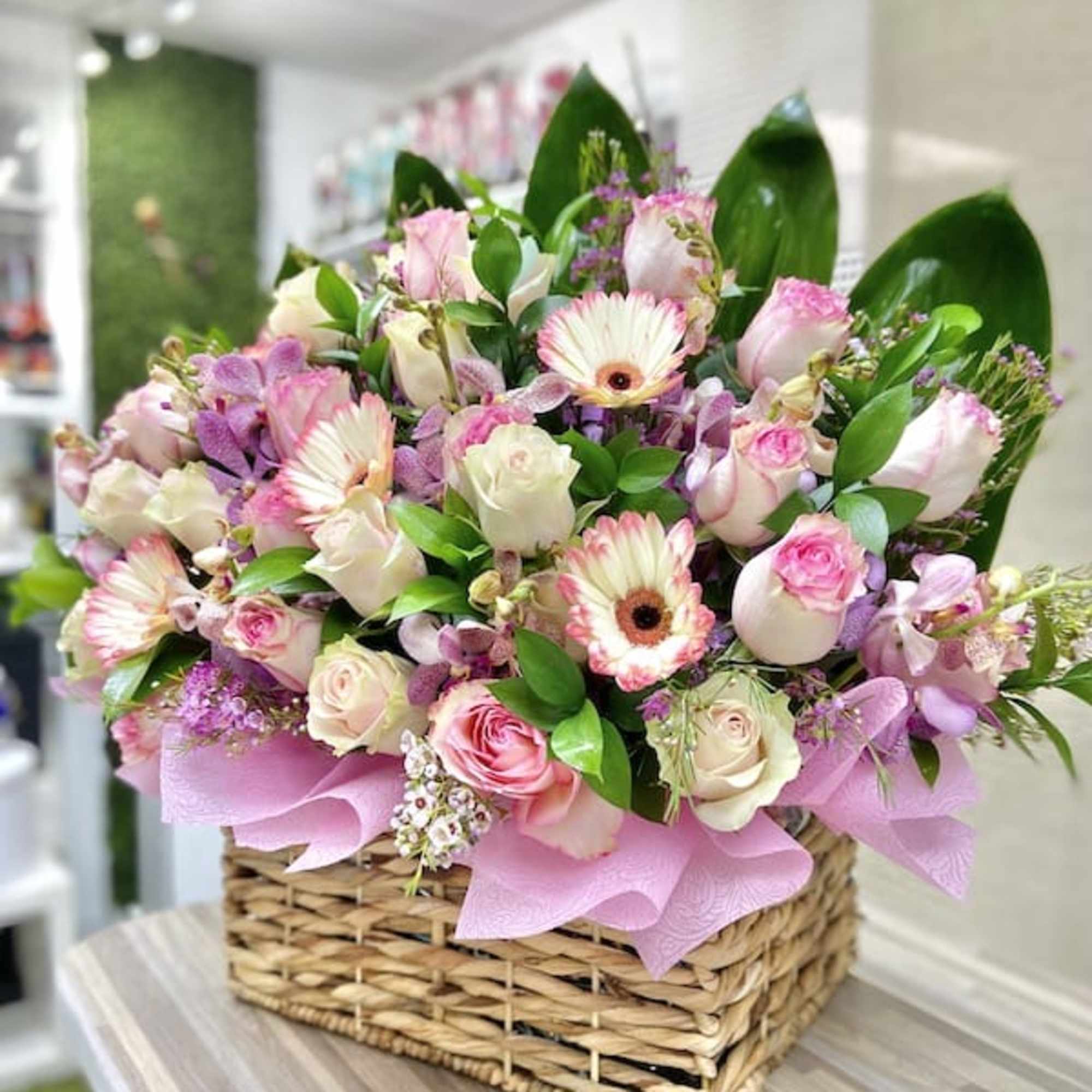 Low basket arrangement of pink gerbera daisies and roses with white accent flowers