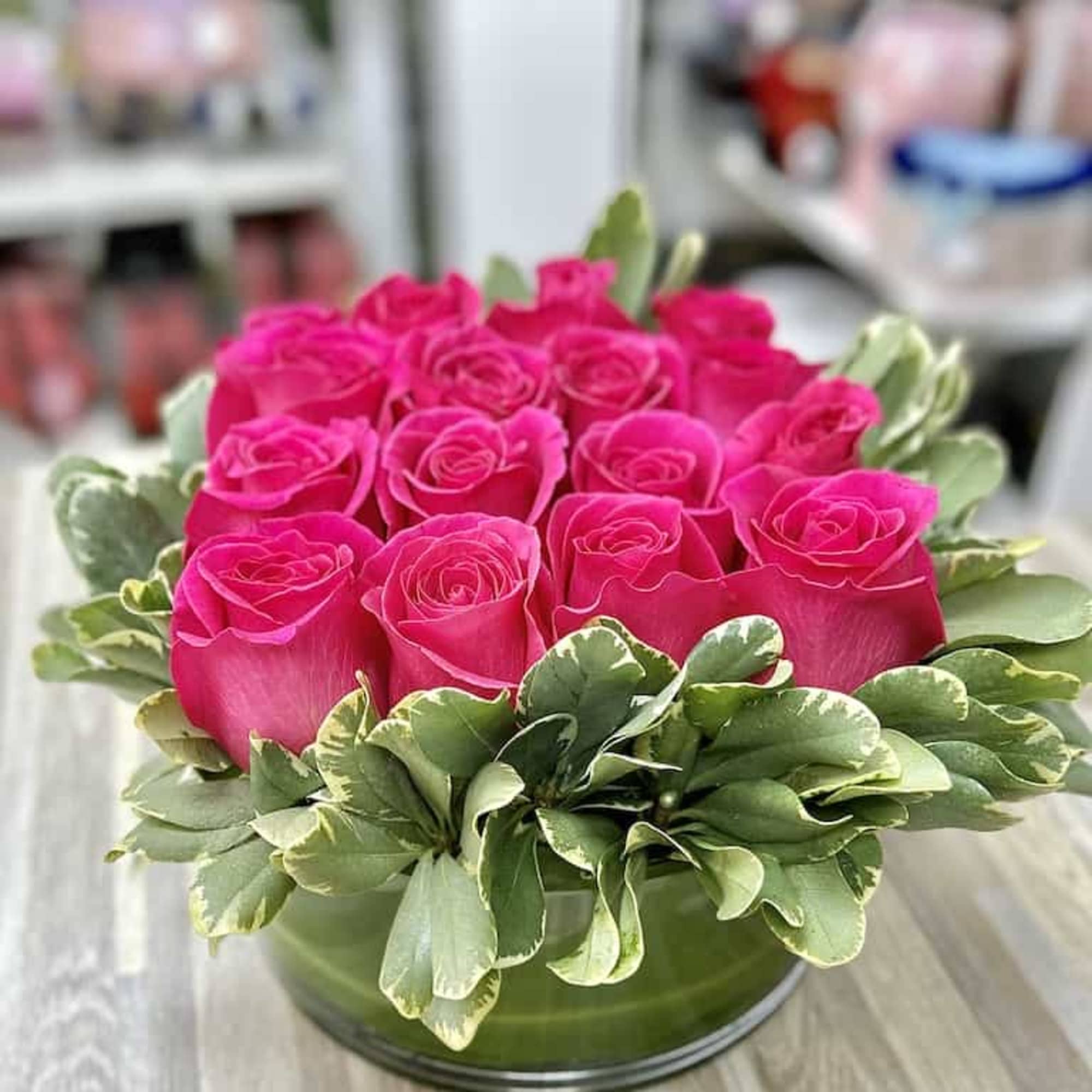 Round arrangement of hot pink roses with a ring of variegated leaves in a low glass vase