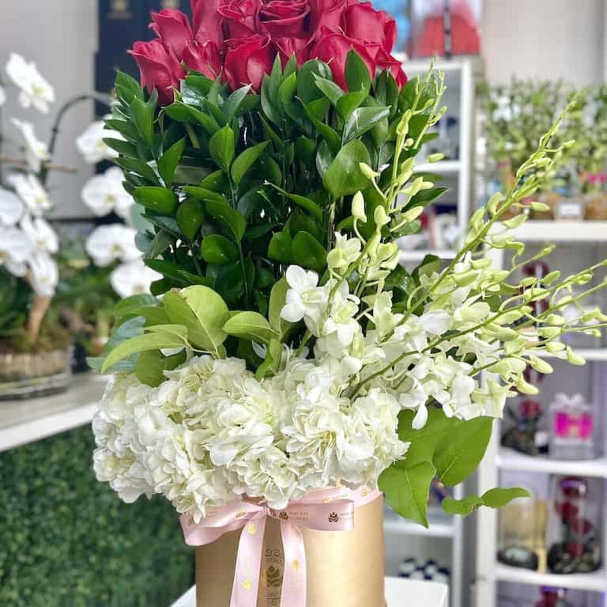Tall arrangement of red roses and white hydrangeas in a gold hatbox with pink ribbon