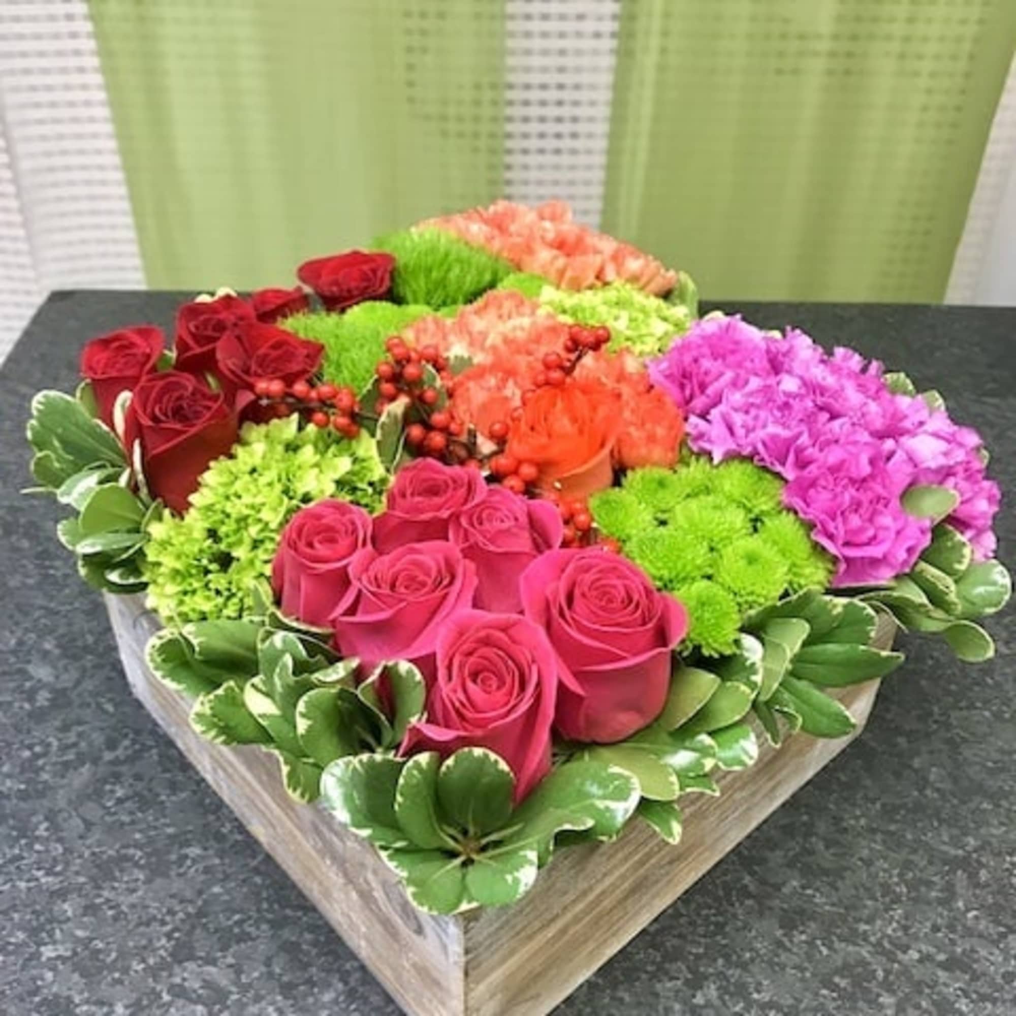 Square box arrangement of pink and red roses, green mums, orange carnations, and pink blooms in color-blocked sections