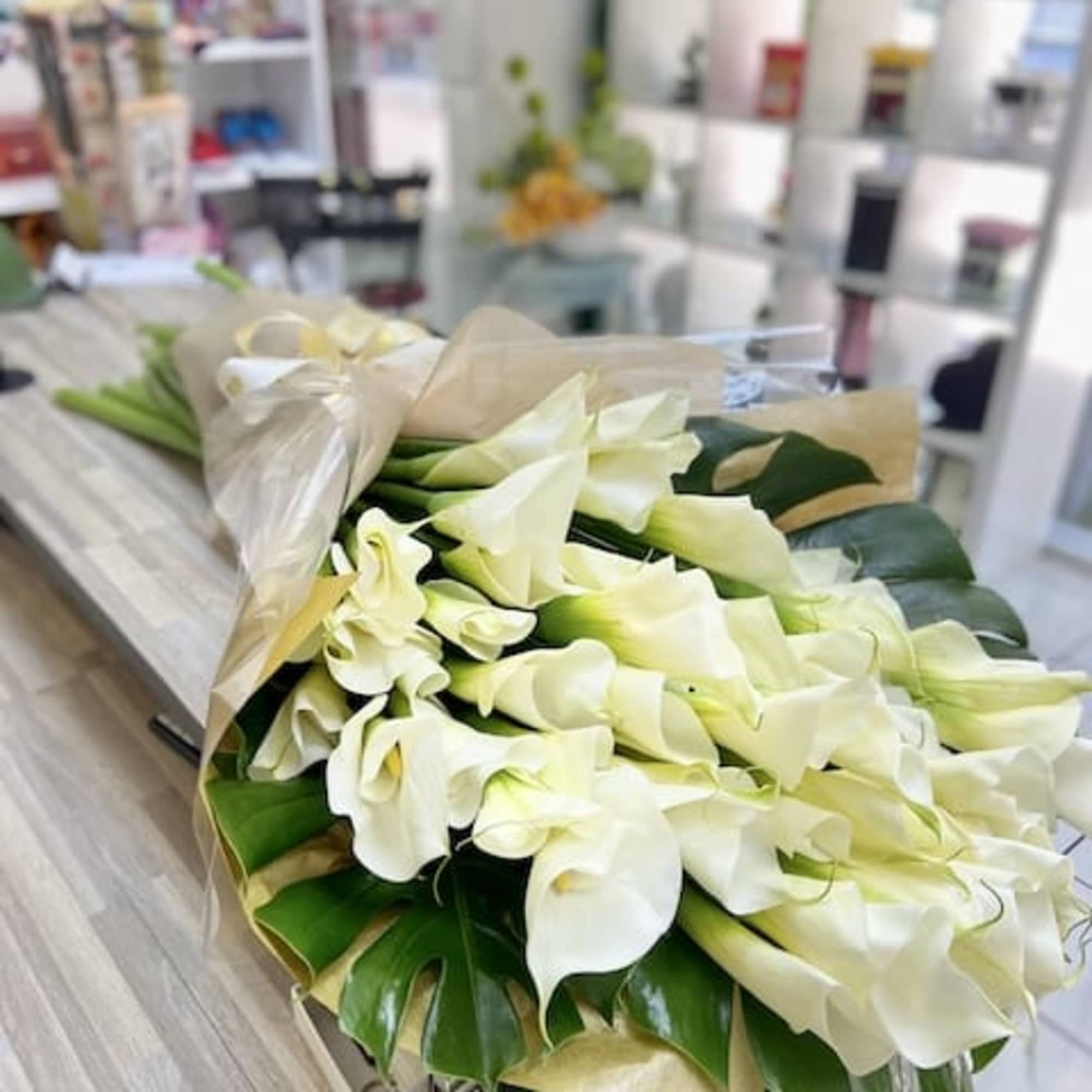 Large wrapped bouquet of white calla lilies with big green tropical leaves on a shop counter