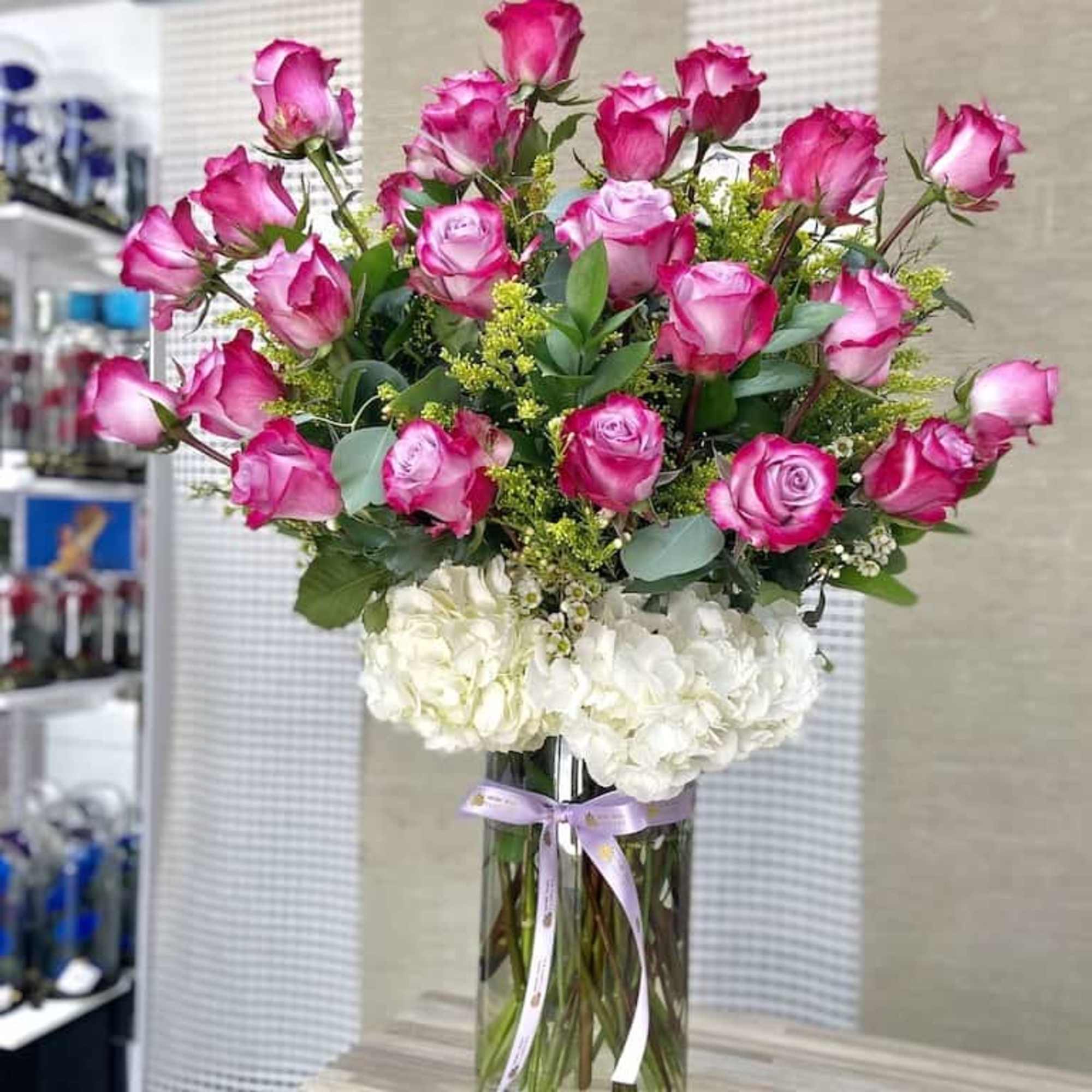 Tall arrangement of pink roses and white hydrangeas in a clear glass vase with a ribbon bow