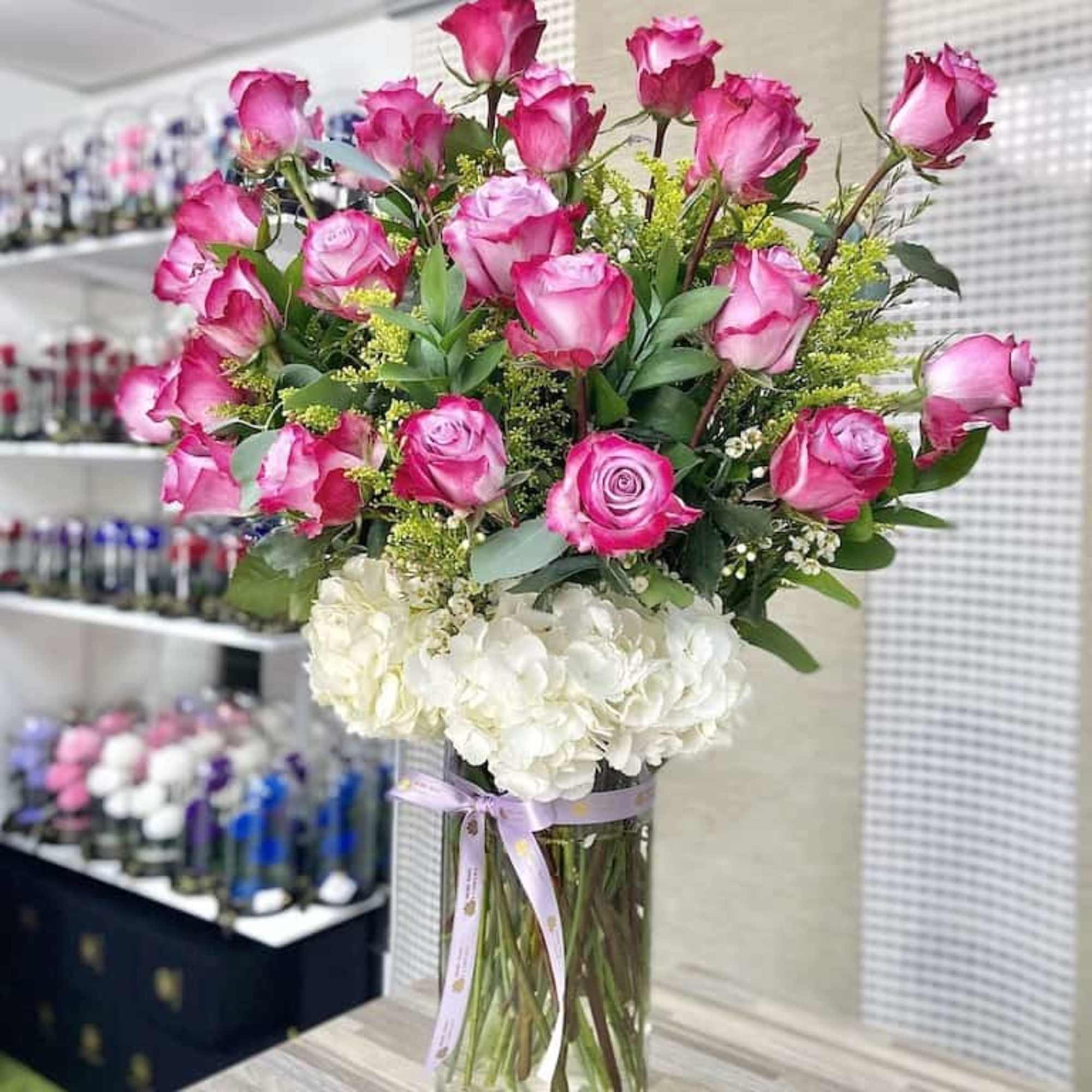 Tall glass vase with pink roses above white hydrangeas and yellow filler flowers.