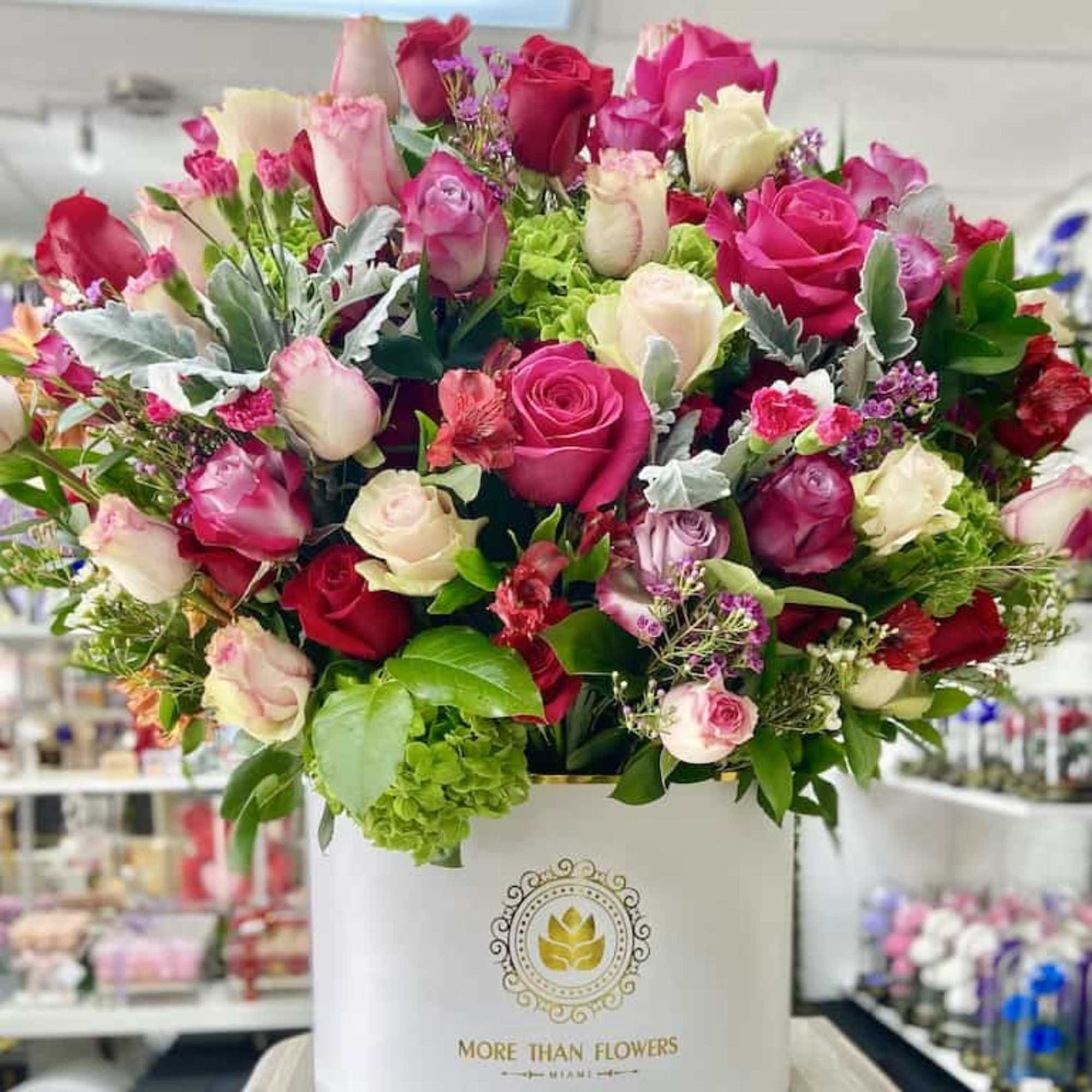 Large hatbox arrangement of pink, red, and cream roses with green hydrangea in a white round box.