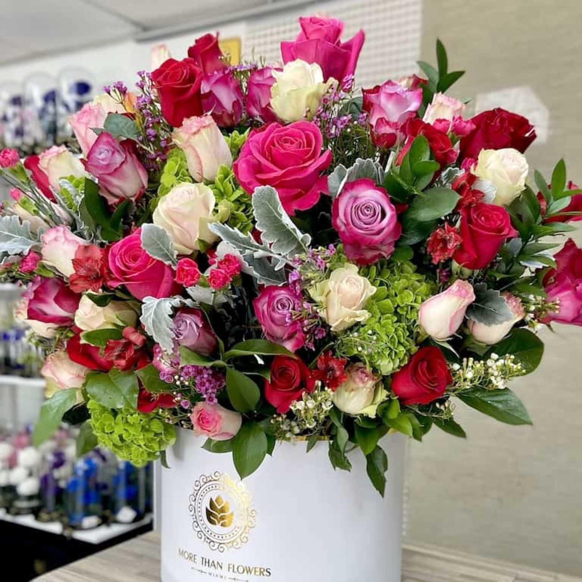 Large arrangement of red, pink, and ivory roses with green accent blooms in a white hatbox container