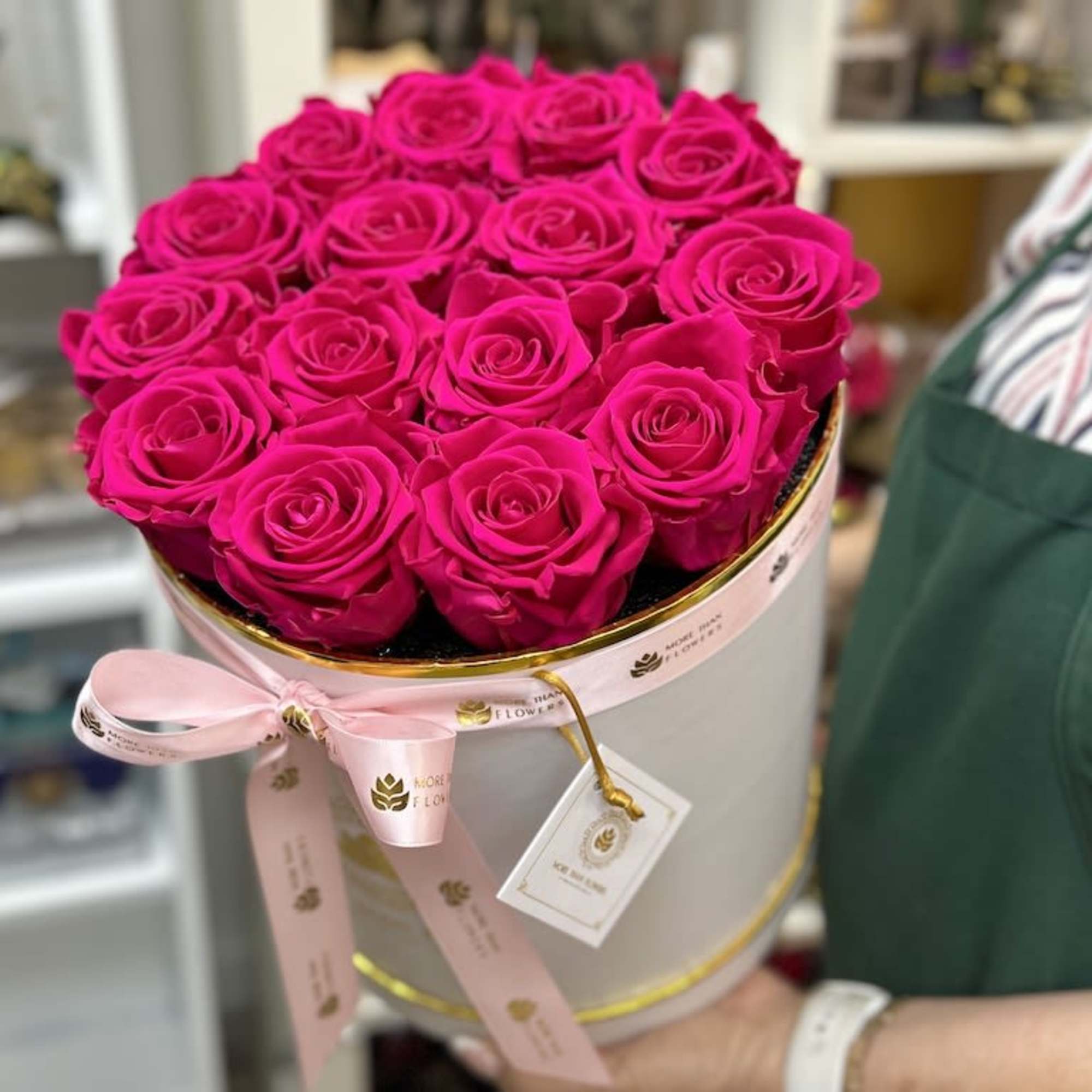 Round white hatbox filled with tightly packed hot pink roses and tied with a pale pink ribbon