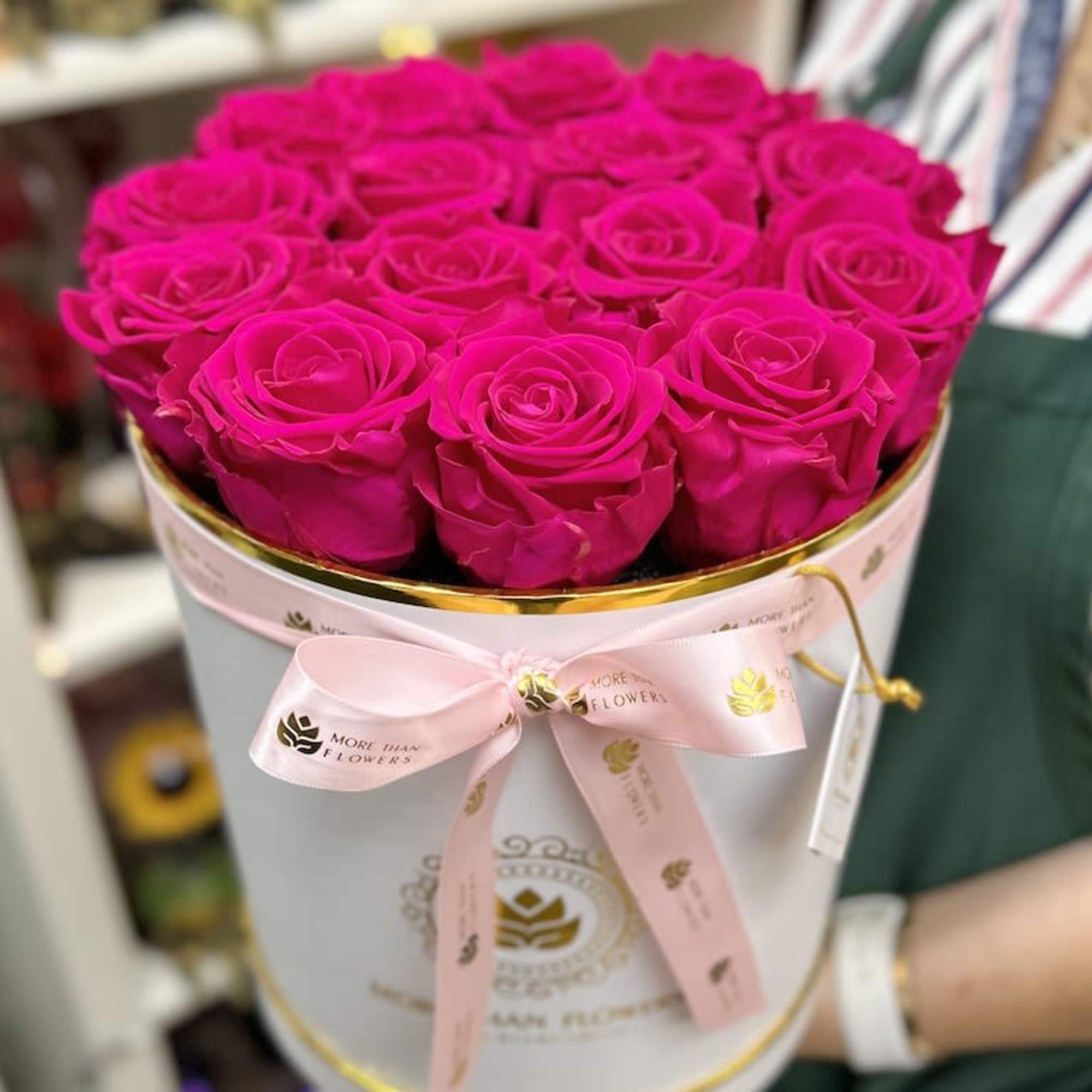 Round white hatbox filled with bright fuchsia roses and tied with a pink ribbon.