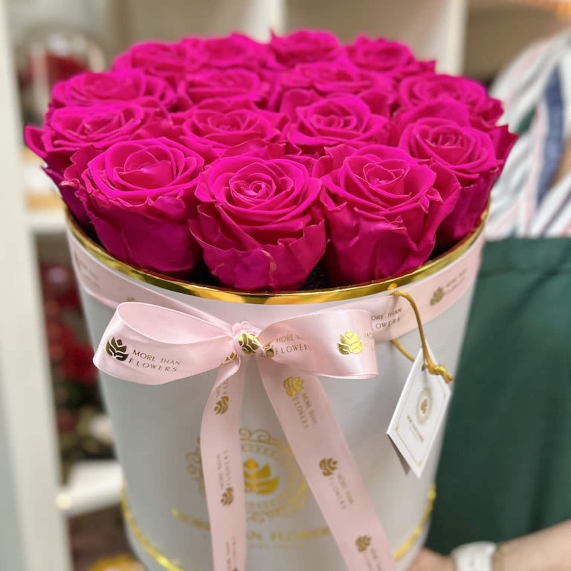 Round white hatbox filled with tightly packed hot pink roses and tied with a pink ribbon.