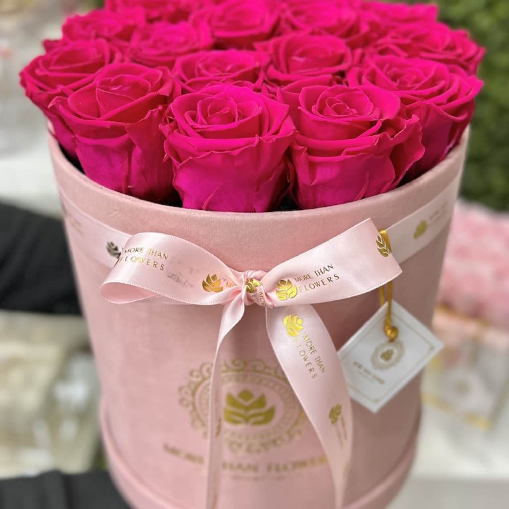 Hot pink roses arranged tightly in a round pink hat box with ribbon and logo