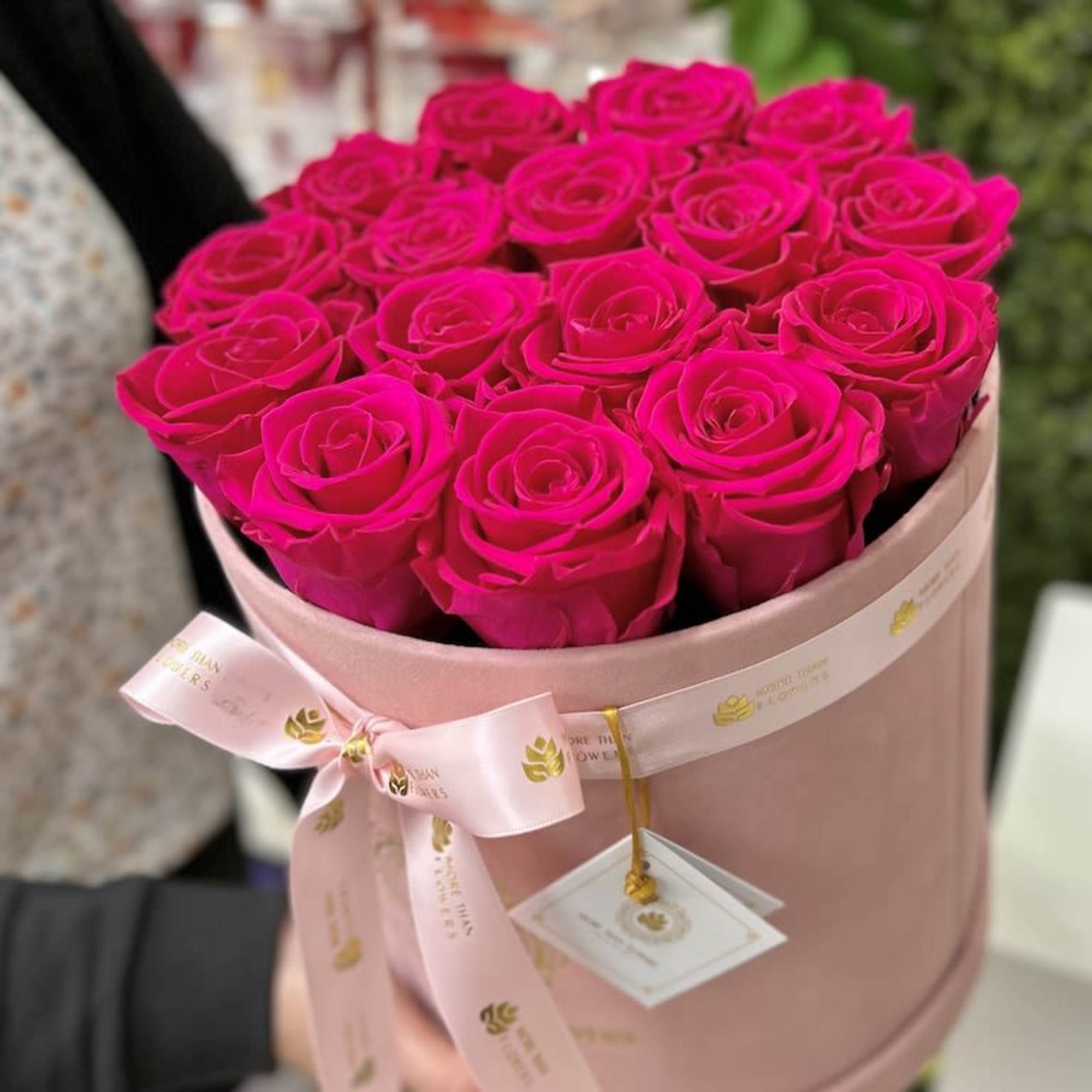 Bright pink roses arranged tightly in a round blush hat box with a pink ribbon and gift tag.