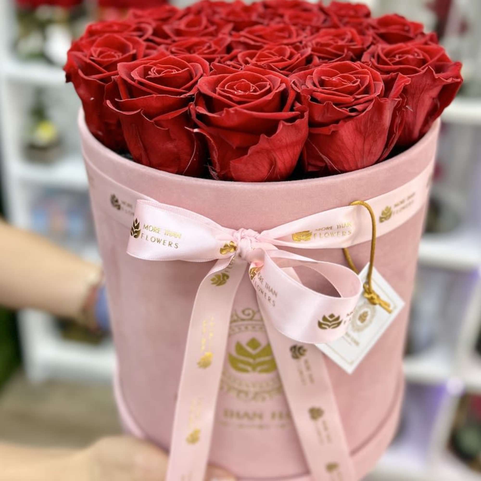Round pink hat box filled with tightly packed red roses and tied with a pink ribbon