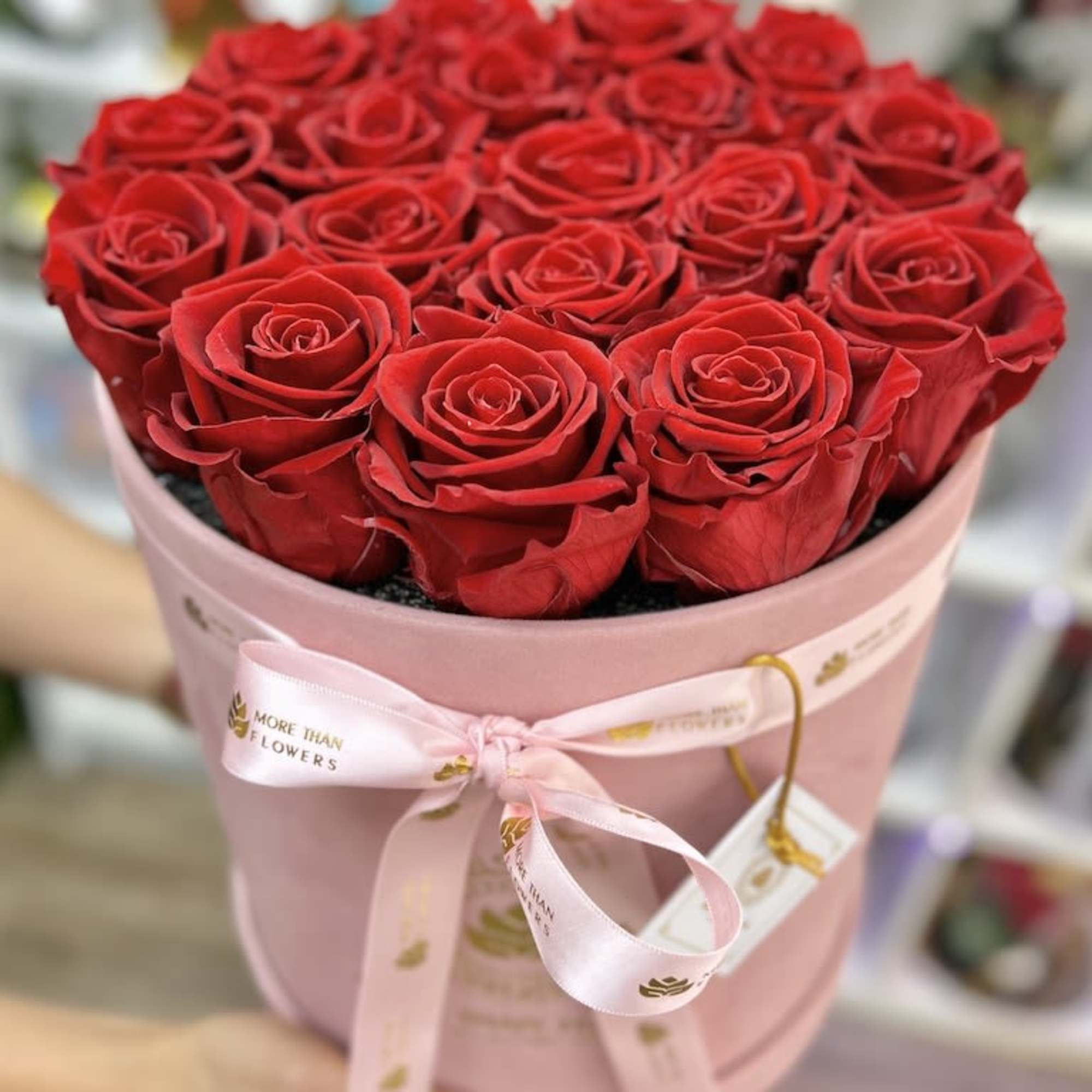 Round pink hatbox filled with tightly packed red roses and tied with a pink ribbon