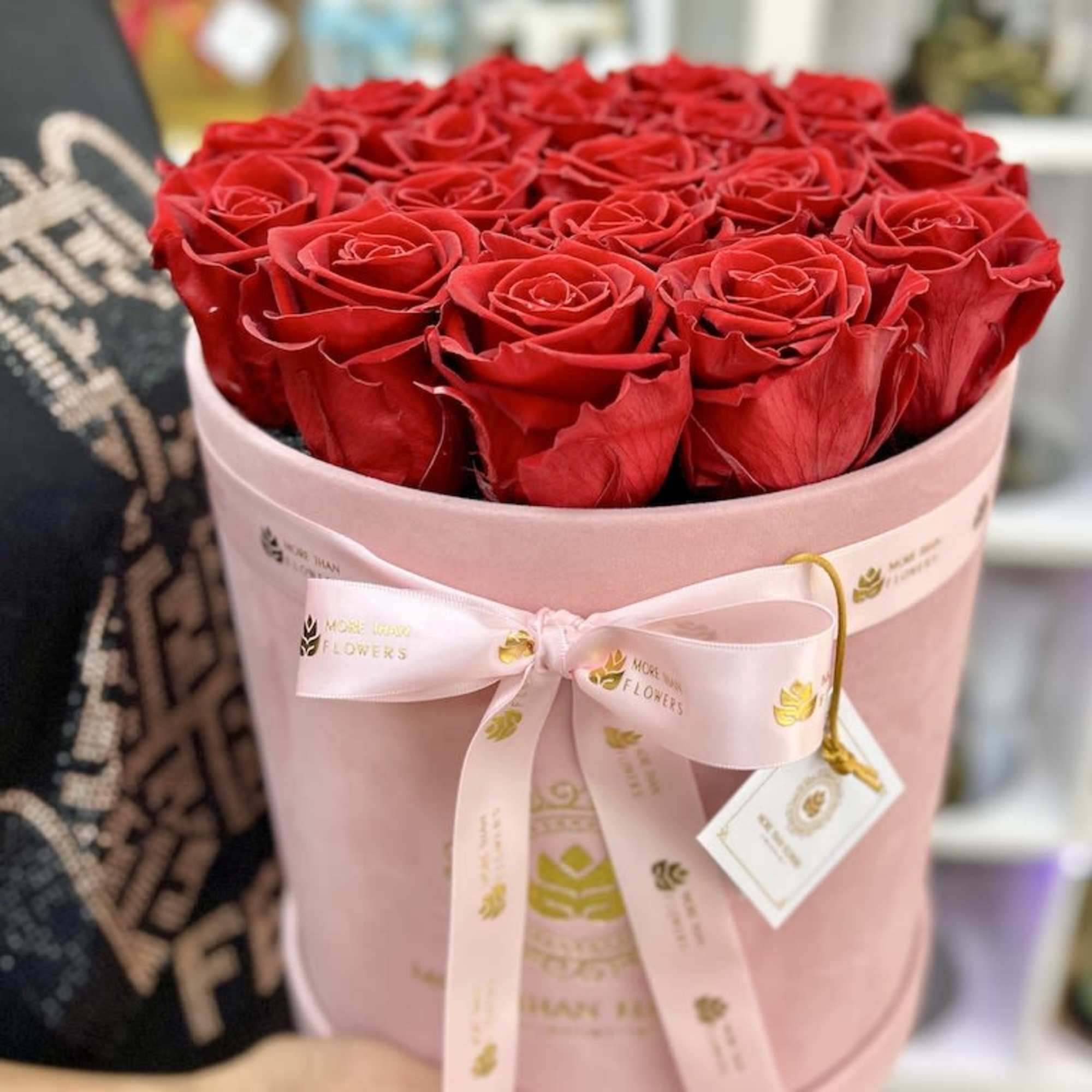 Round box of red roses in a pink hatbox with ribbon and tag