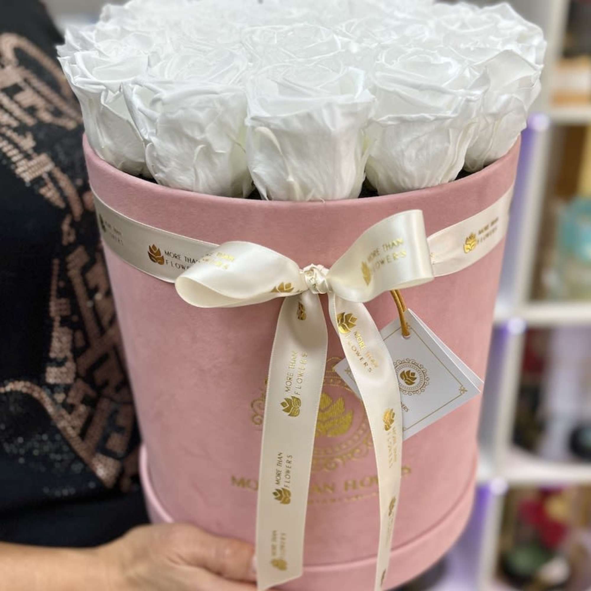 Round pink hat box filled with tightly packed white roses and tied with a cream ribbon