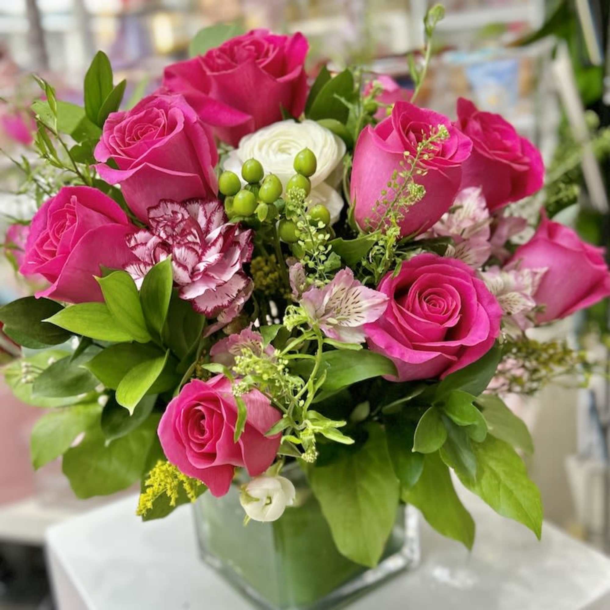 Square vase arrangement of hot pink roses with white accent flowers and berries