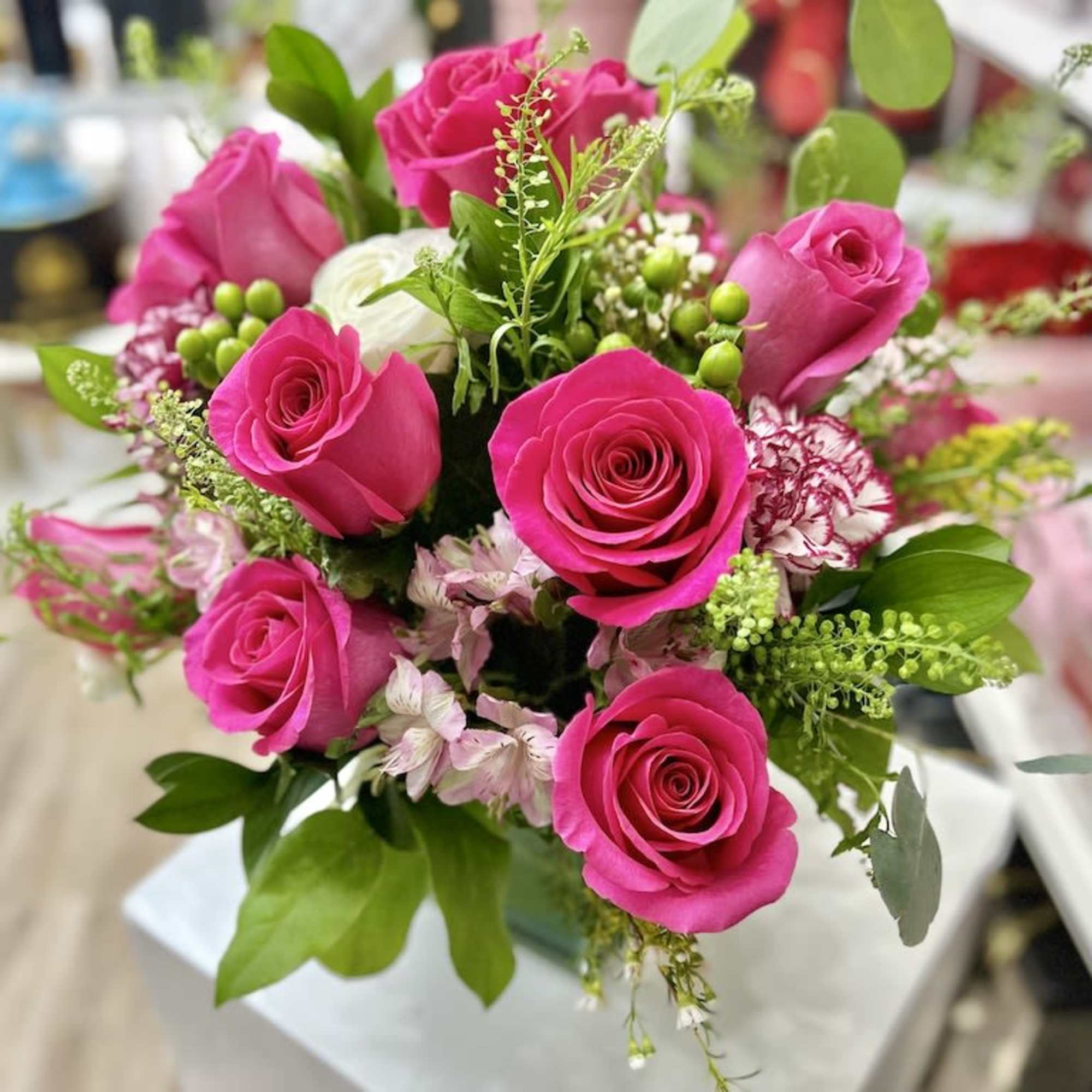 Arrangement of bright pink roses with pale pink accent flowers in a clear glass vase