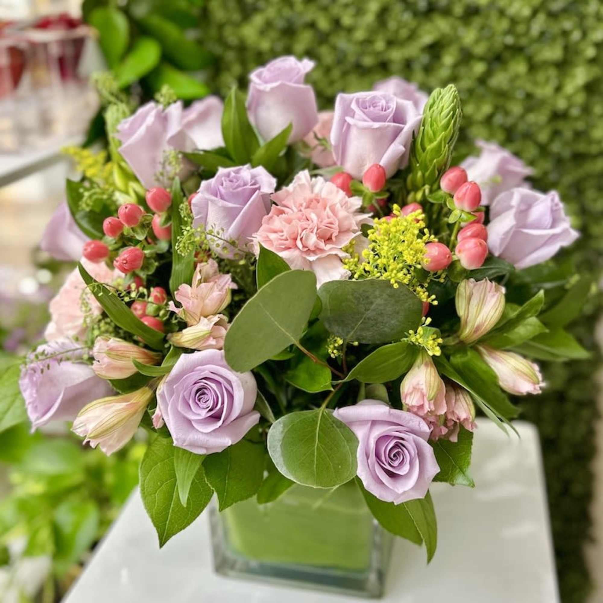 Lavender roses and pink carnations with berries in a square glass vase