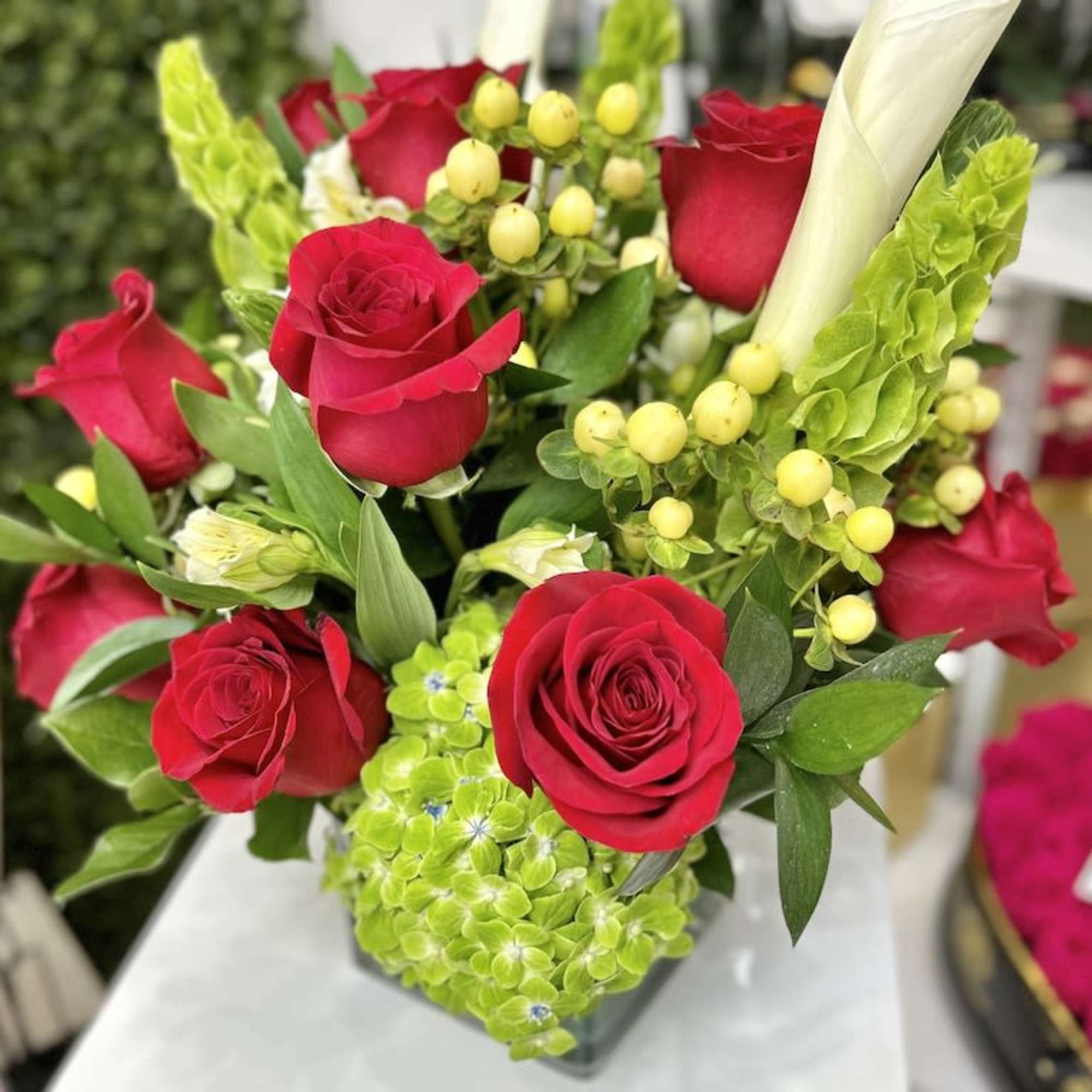 Compact arrangement of red roses, white calla lilies, and green hydrangeas in a square glass vase