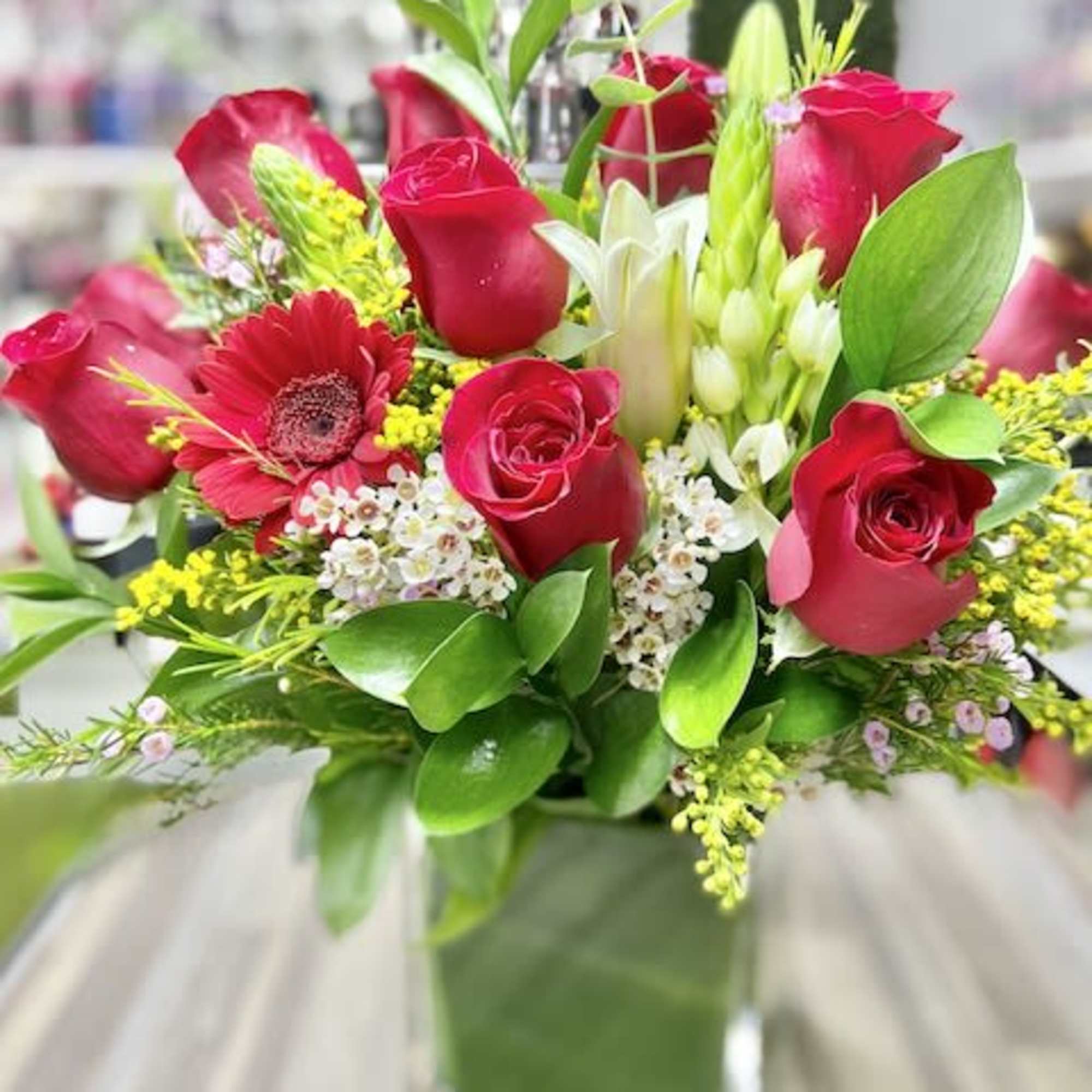 Red rose and white lily arrangement with filler flowers in a square glass vase