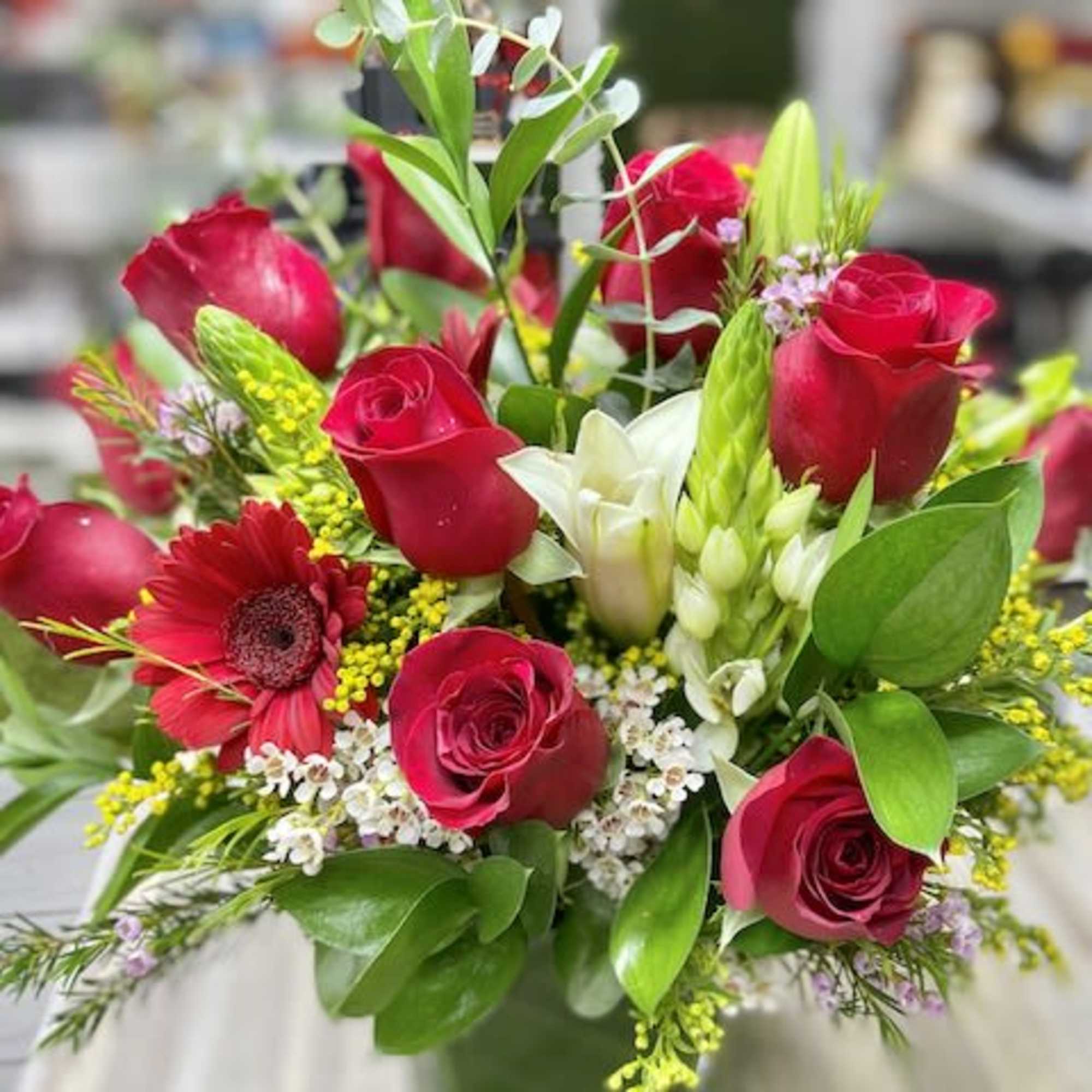 Red rose and white lily arrangement with accent blooms in a clear glass cube vase
