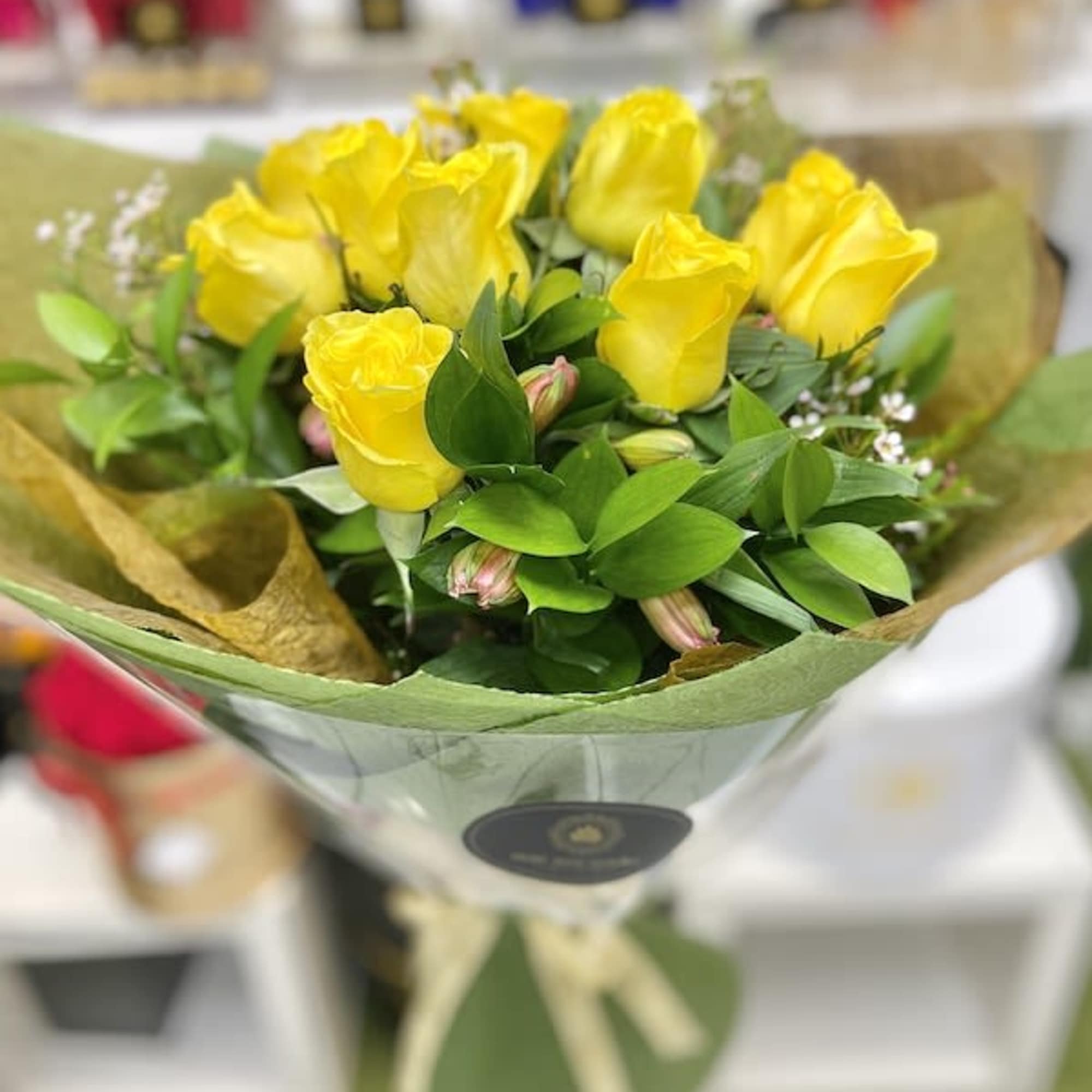 Hand-tied bouquet of yellow roses wrapped in green and brown paper with a ribbon