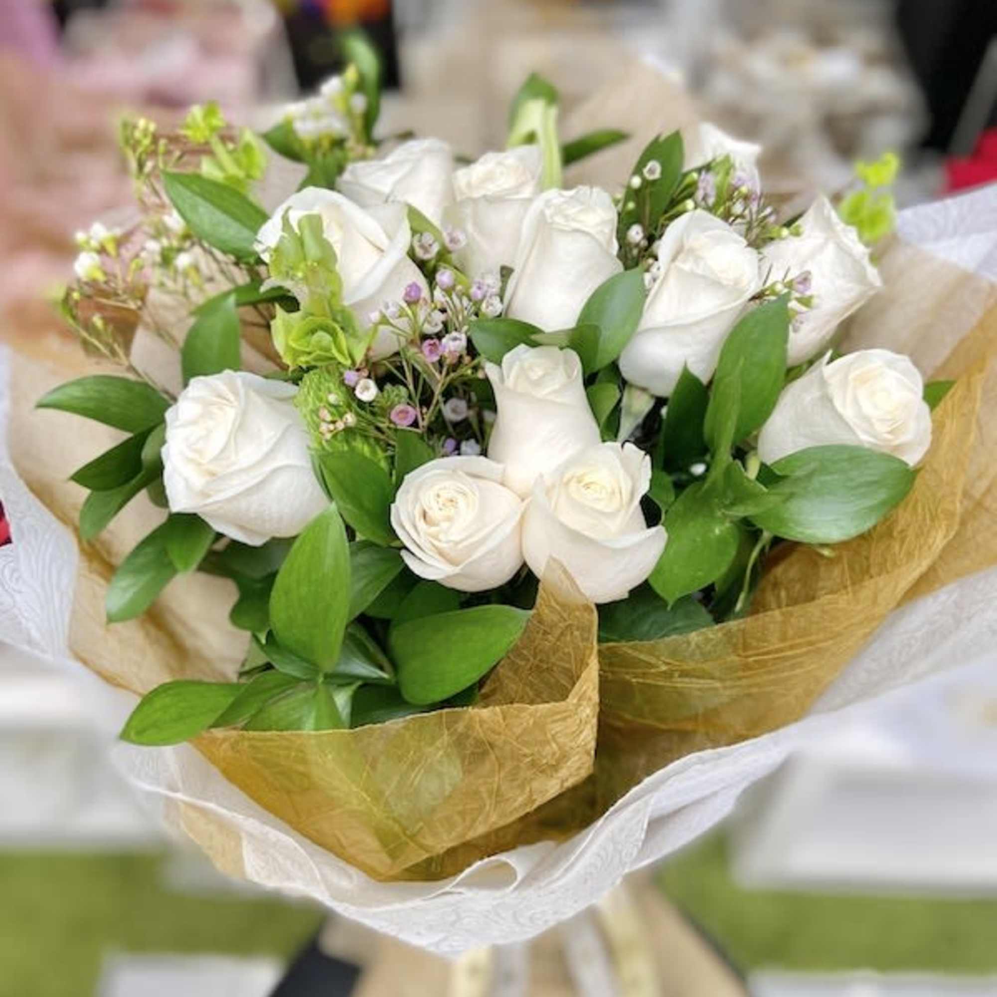 Bouquet of white roses with small filler flowers wrapped in white and gold paper