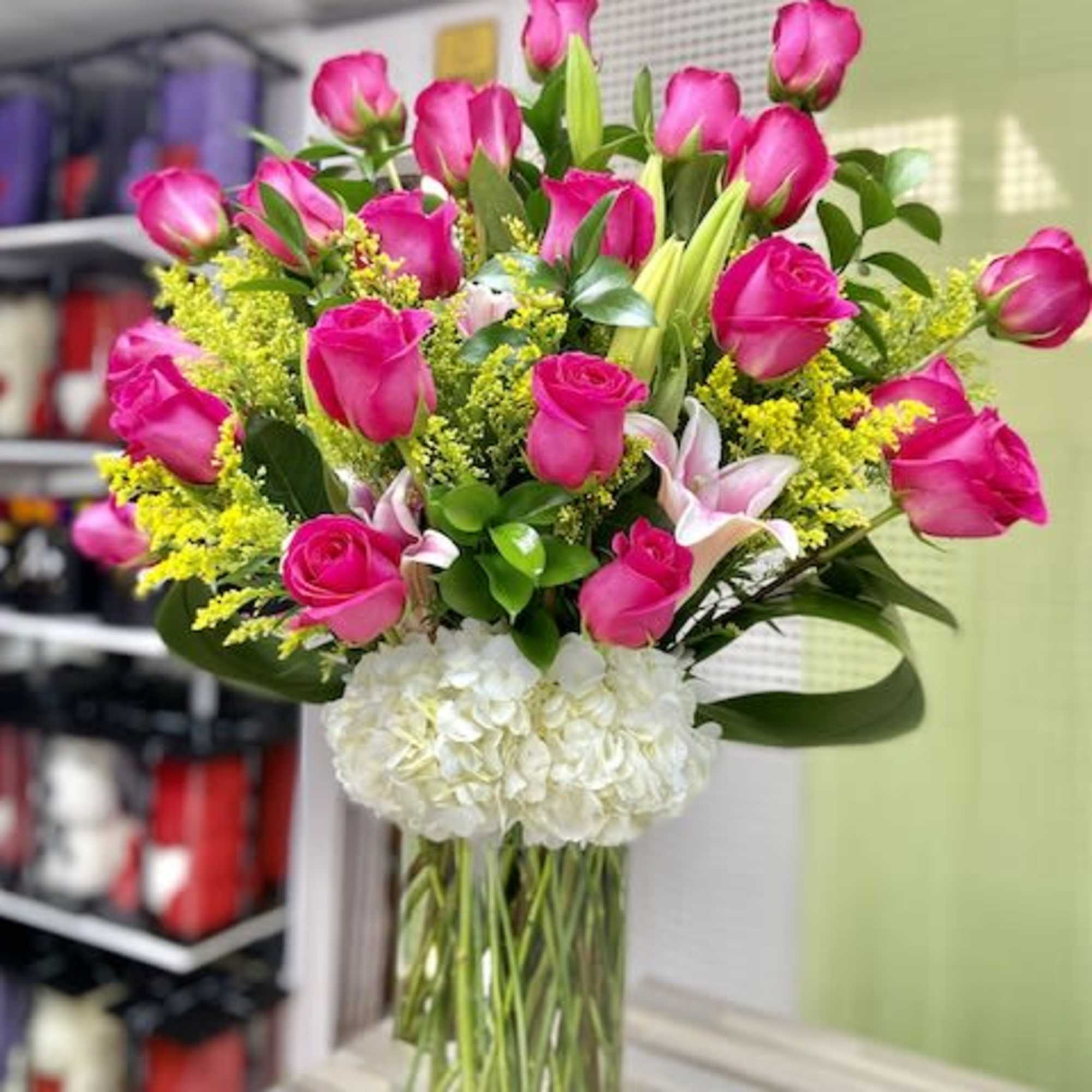 Tall arrangement of hot pink roses, lilies, and white hydrangeas in a clear glass vase