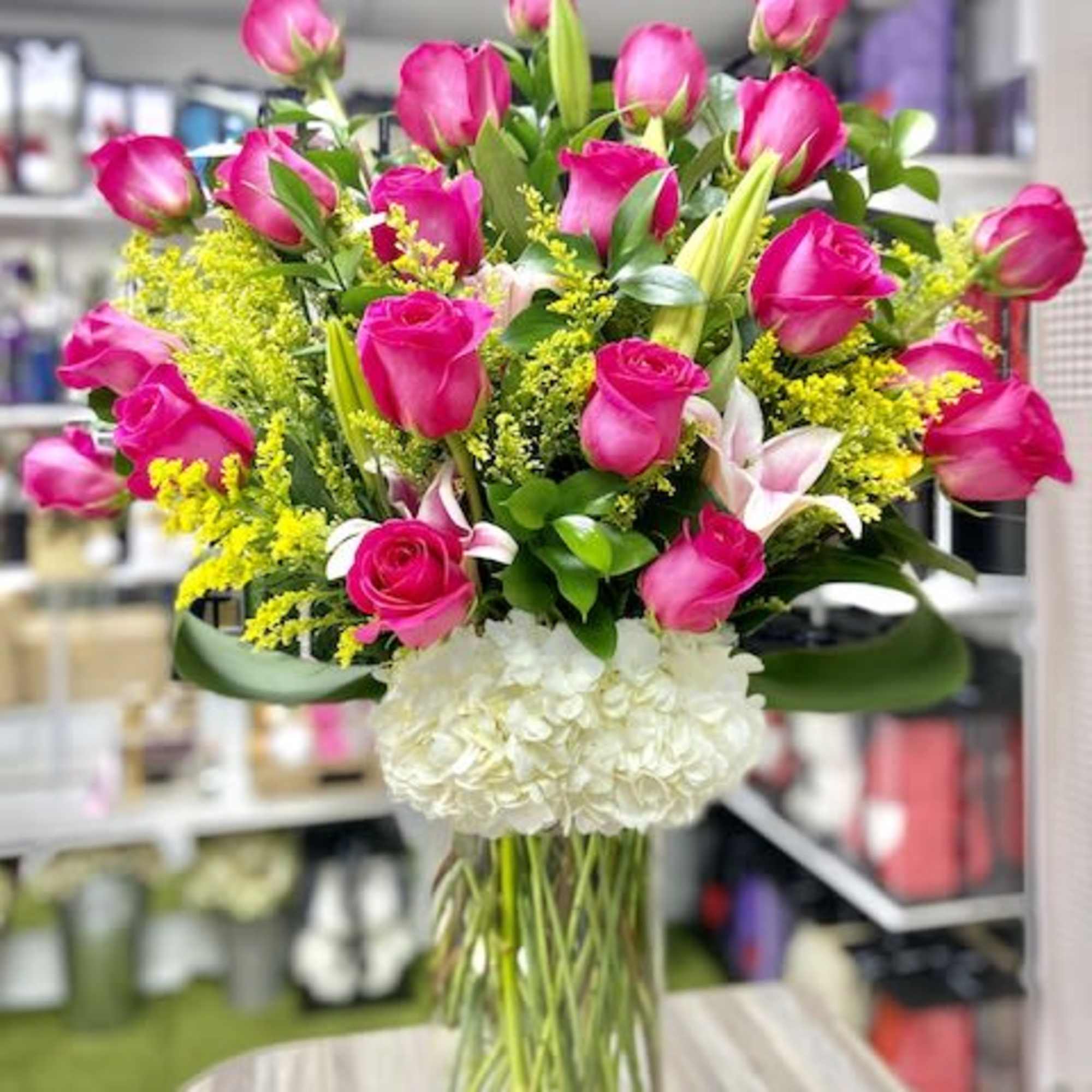 Tall glass vase of hot pink roses, lilies, and white hydrangeas with yellow filler flowers