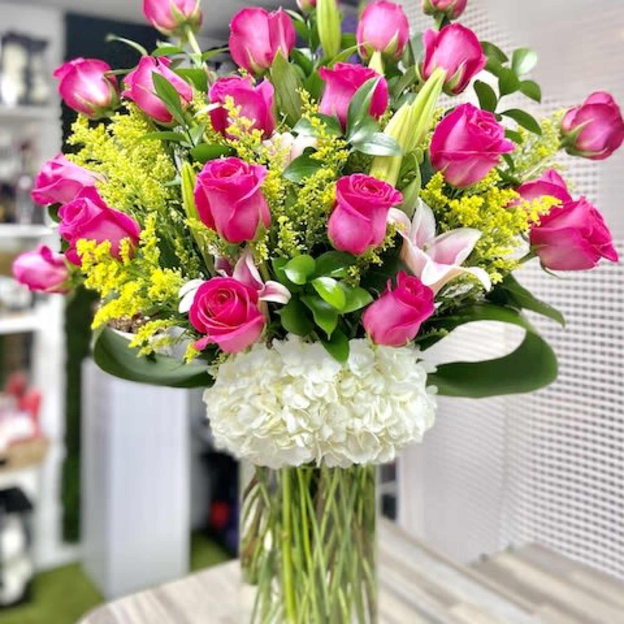 Tall arrangement of hot pink roses, white hydrangeas, and lilies in a clear glass vase