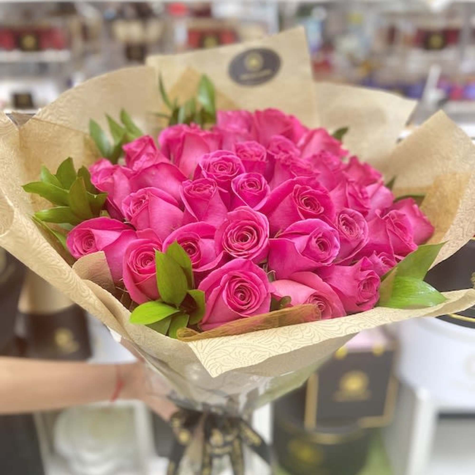 Bouquet of bright pink roses wrapped in tan patterned paper with a black ribbon tie.