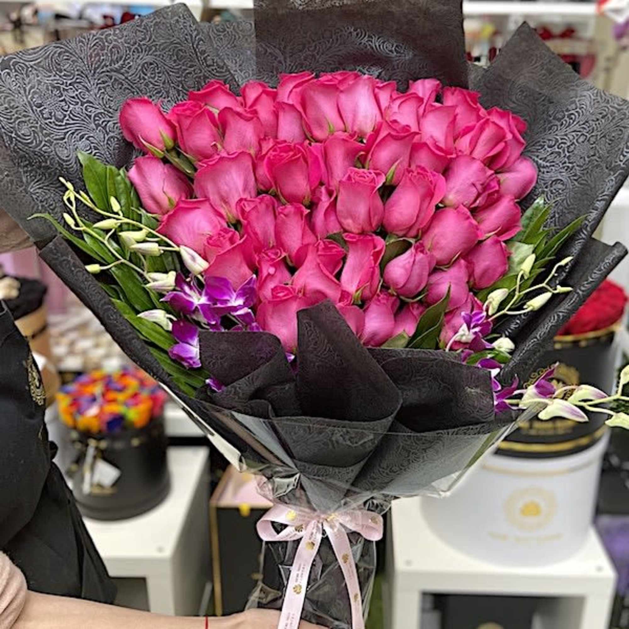 Large bouquet of hot pink roses with purple orchids wrapped in black patterned paper and tied with a pink ribbon