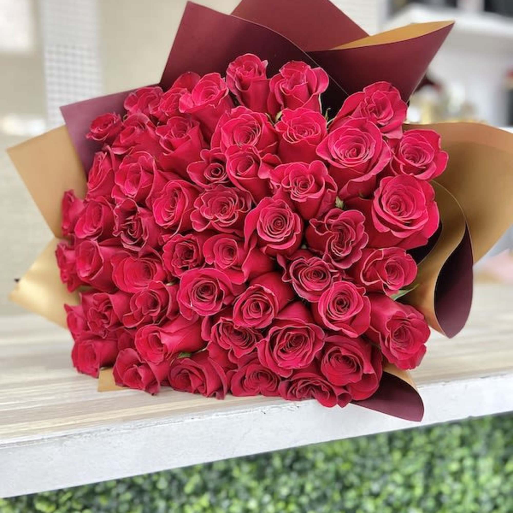Large bouquet of bright pink roses wrapped in burgundy and gold paper