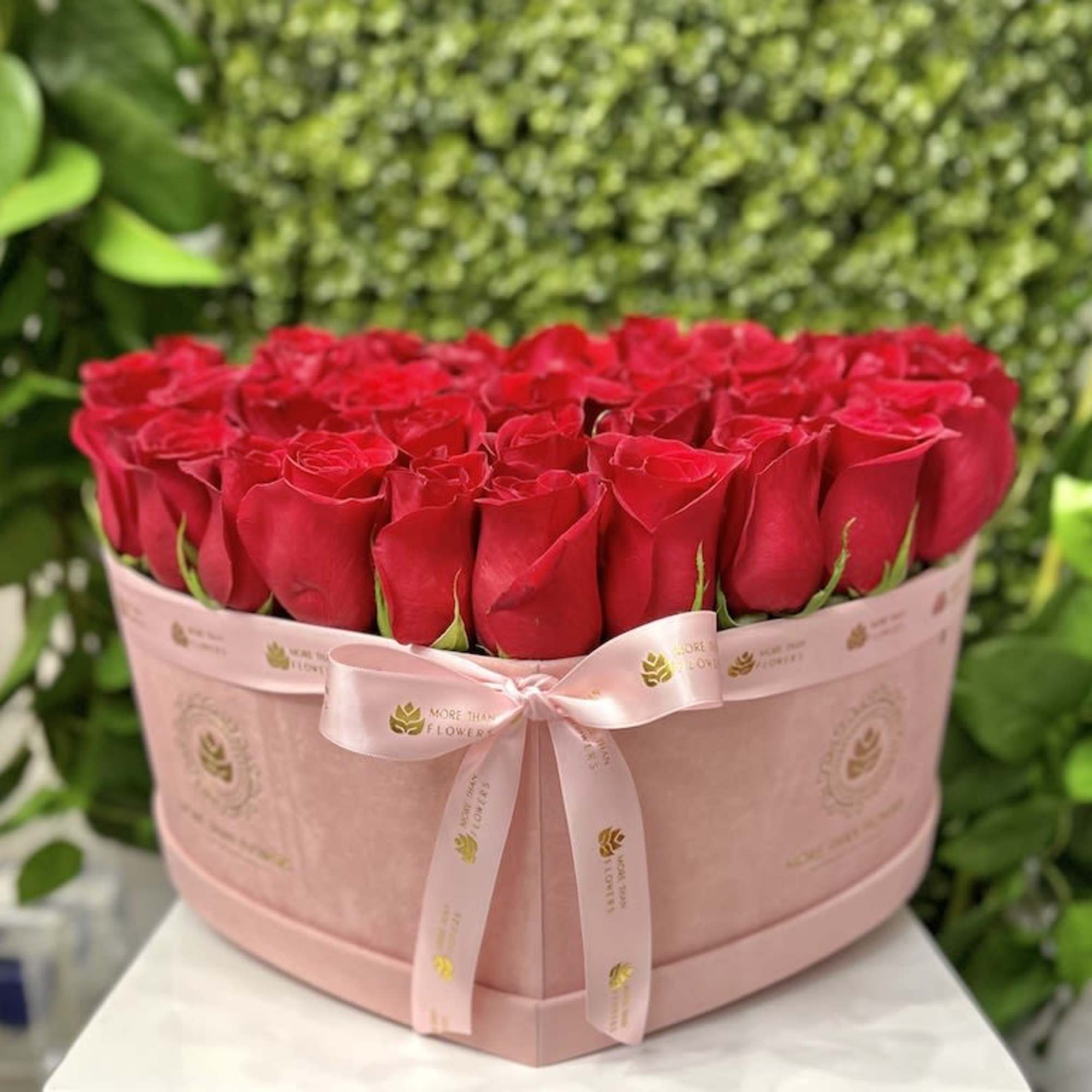 Heart-shaped pink box filled with tightly packed red roses and tied with a pink ribbon.