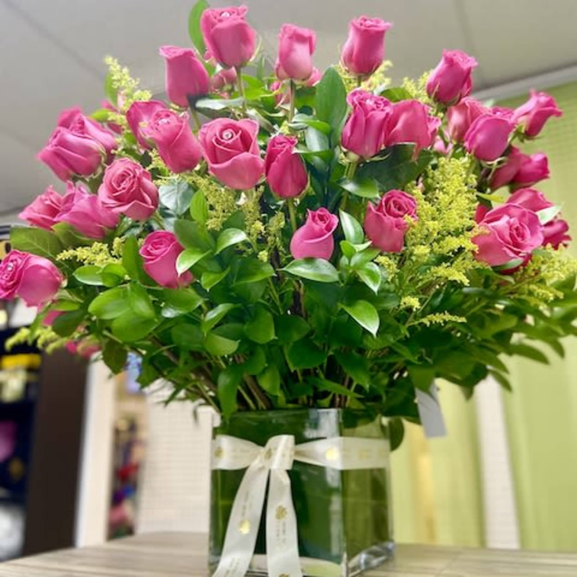 Large arrangement of hot pink roses in a square glass vase with ribbon bow