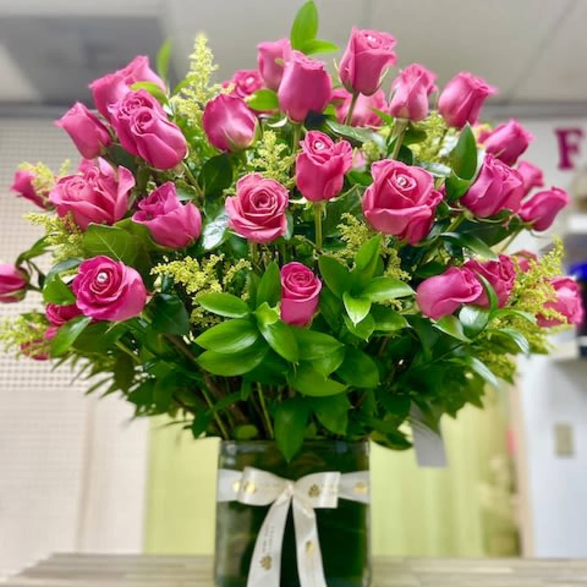 Tall arrangement of bright pink roses in a square glass vase with a white bow