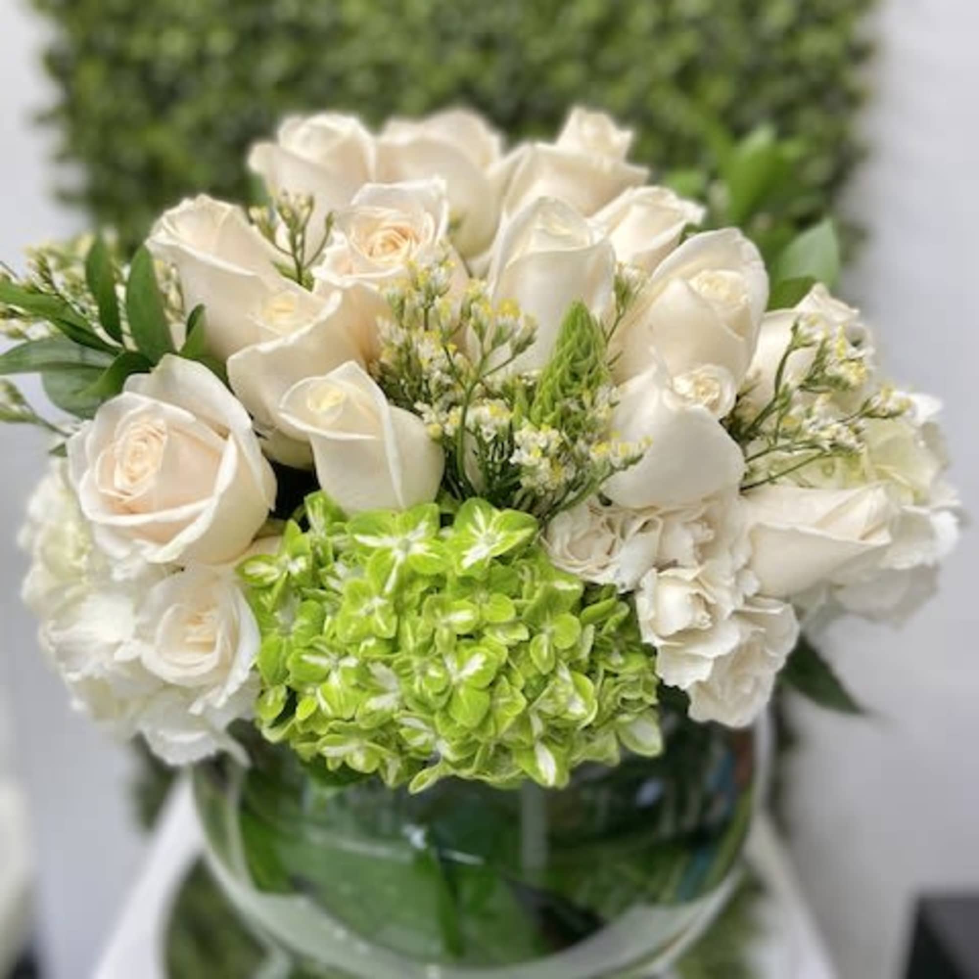 Low round arrangement of ivory roses and green hydrangea in a clear glass bowl vase