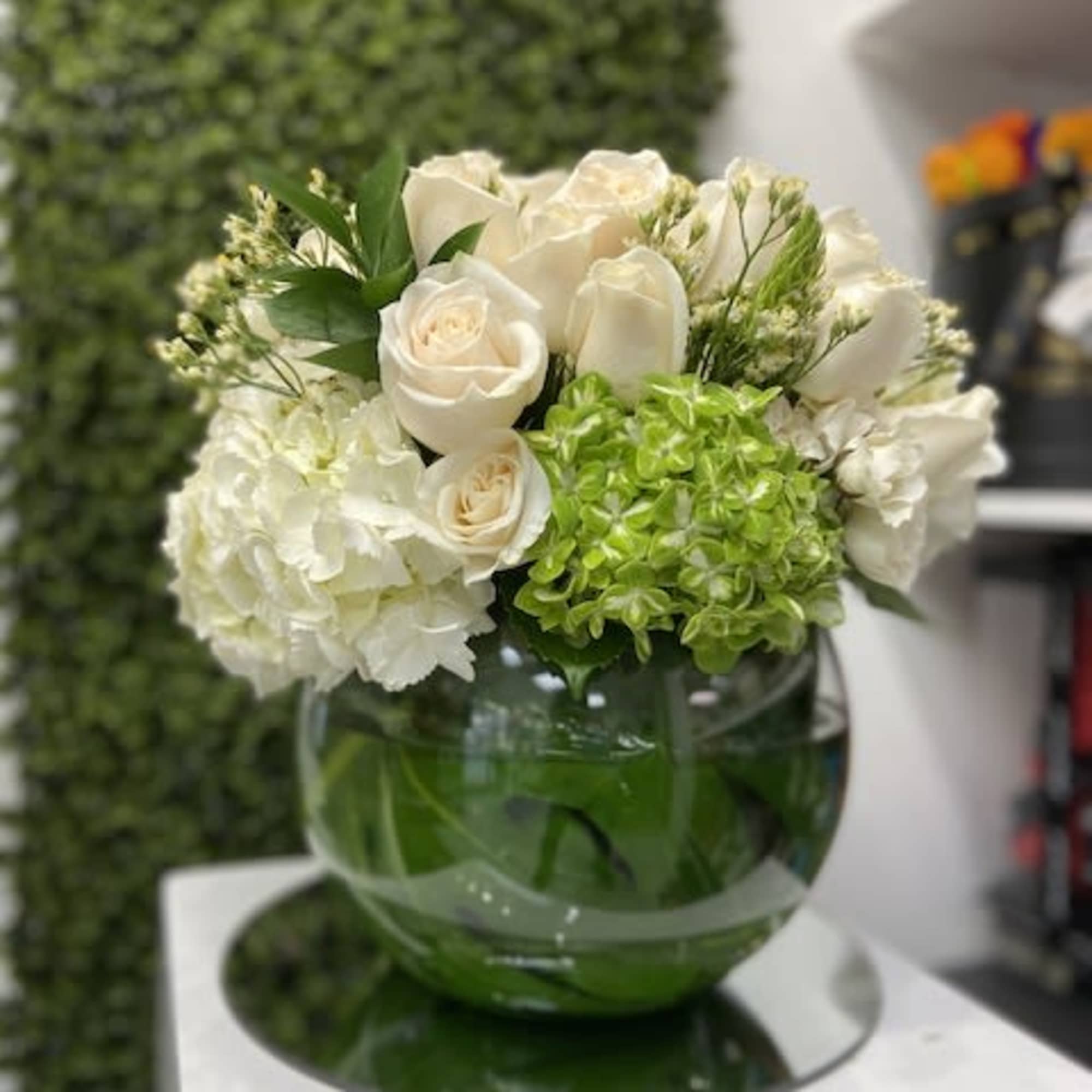 Low round arrangement of white roses and hydrangeas with green accents in a glass bowl vase