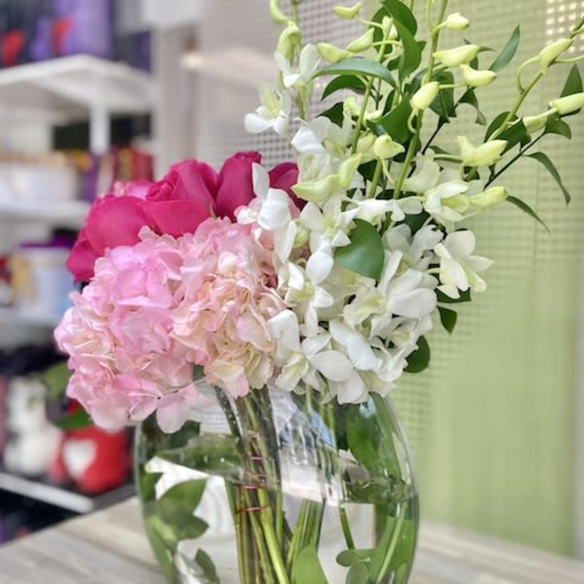 Pink roses, pale hydrangeas, and white orchids in a round glass vase with white stones.